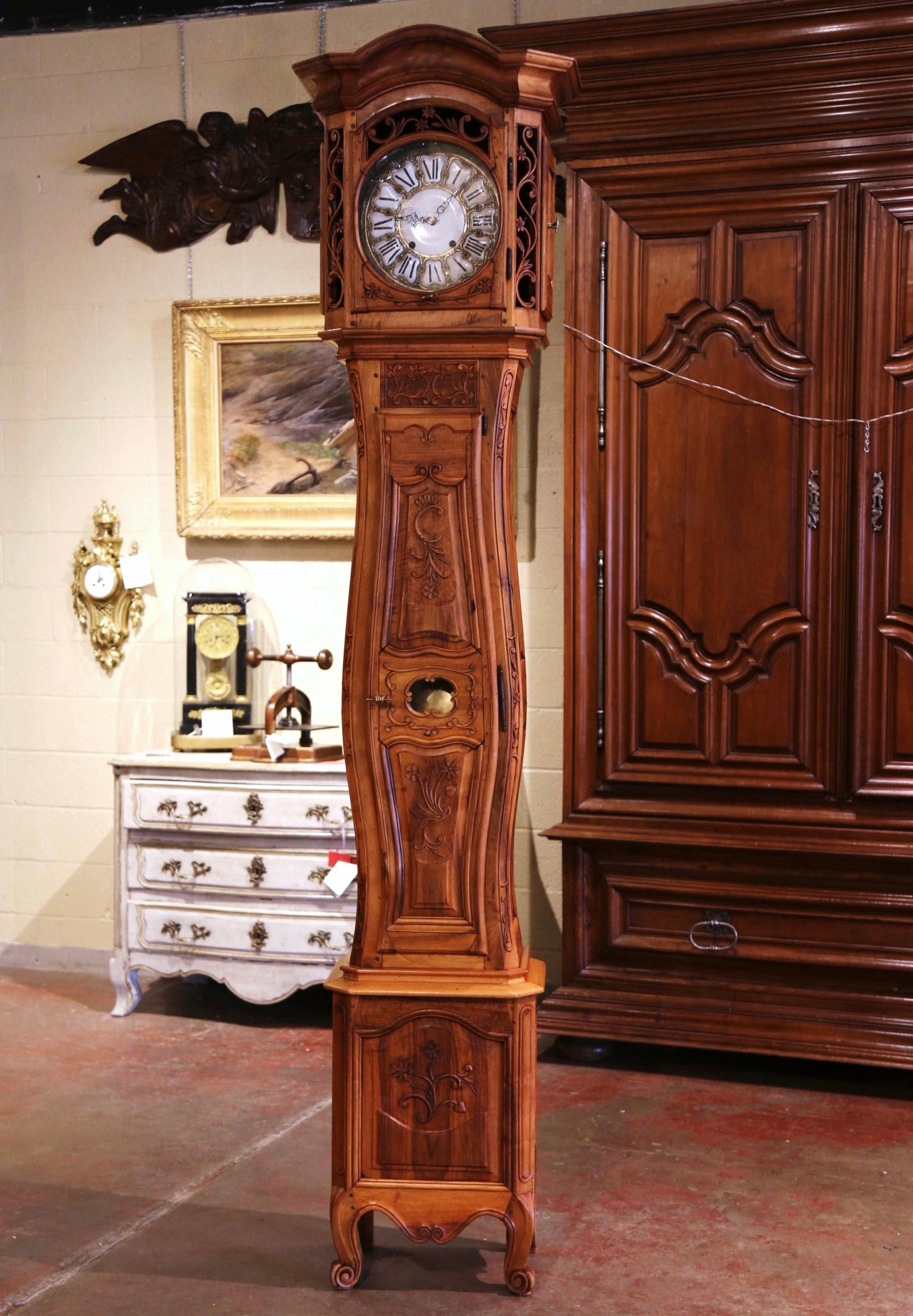 Crafted in Southern France, circa 1880, the antique tall case clock stands on escargot feet under a scalloped apron, and is heavily carved. The cabinet is built in two sections, with beautiful lines including a carved bonnet top, a violin shape body