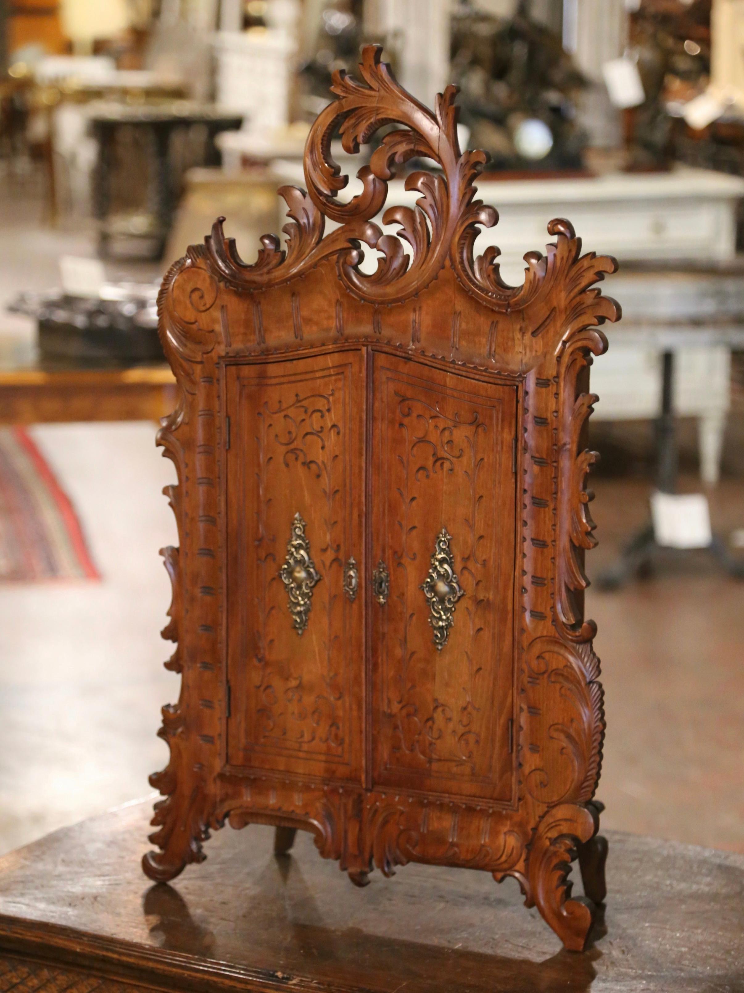 This elegant and heavily carved antique vitrine was crafted in France, circa 1880. The hanging cabinet with pierced shell cartouche at the pediment, stands on acanthus leaf form legs over a scalloped apron decorated with a center floral motif; it is