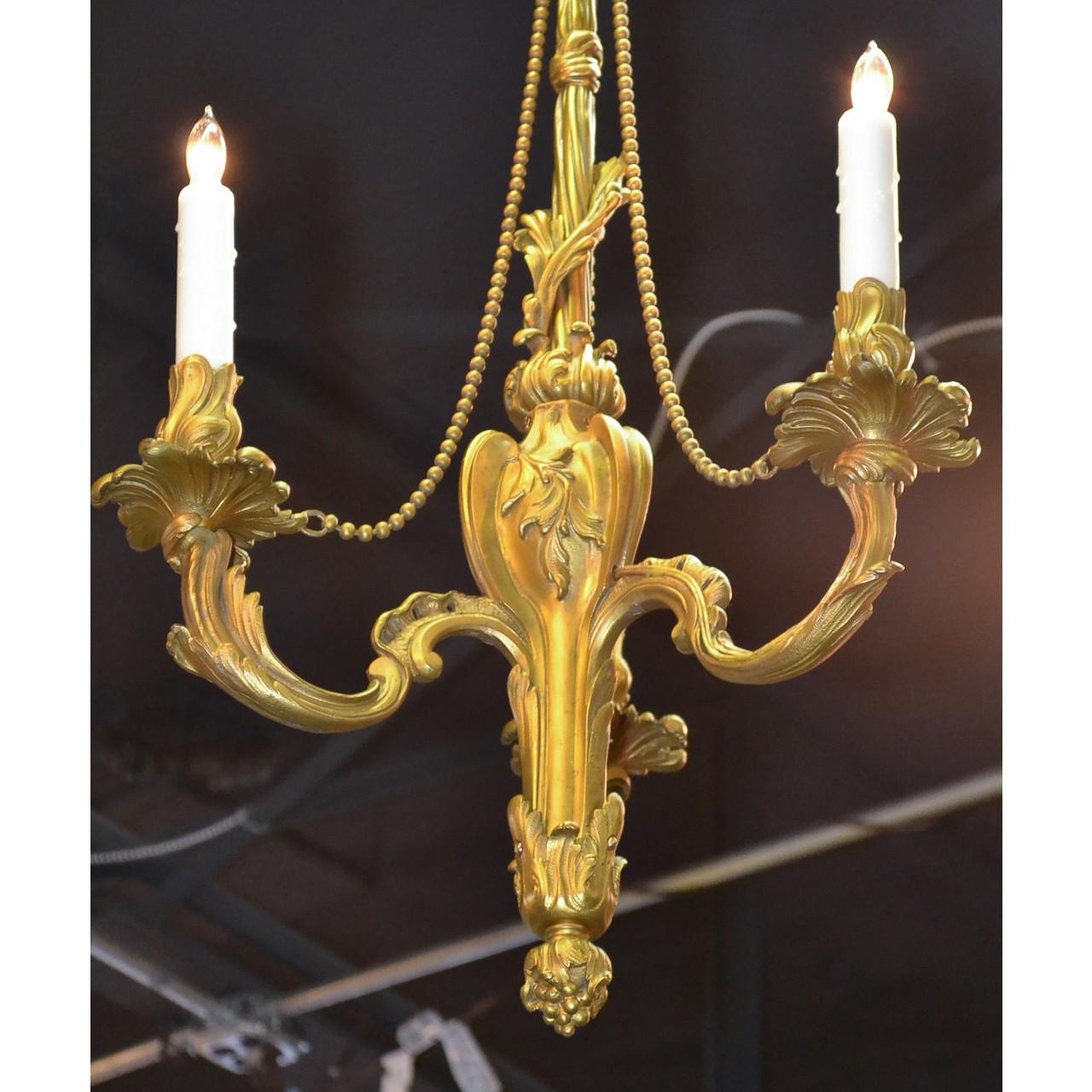 Beautifully understated 19th century French Louis XV style gold-gilded bronze chandelier with a foliate canopy and a unique knotted-sash and leaf accented stem. Lovely draped bead strands lead to three acanthus motif scrolled arms having leaf-spray