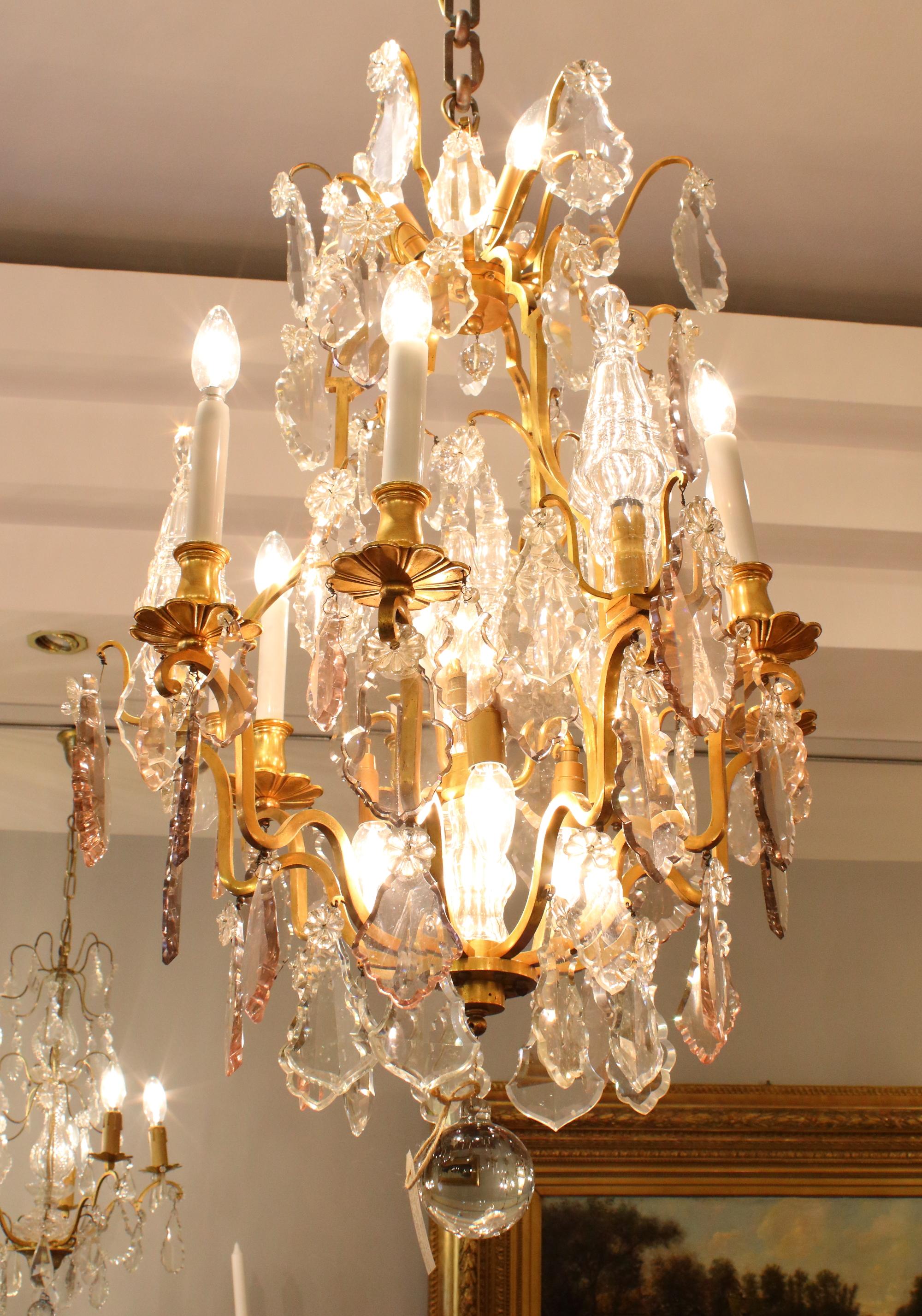 A large Louis XV style 16-light crystal-cut chandelier decorated overall in scalloped crystal glass pendalogues, partially colored, with flower jewels and impressive moulded lit baluster pinnacles. The open pear- or basket shaped frame supports six