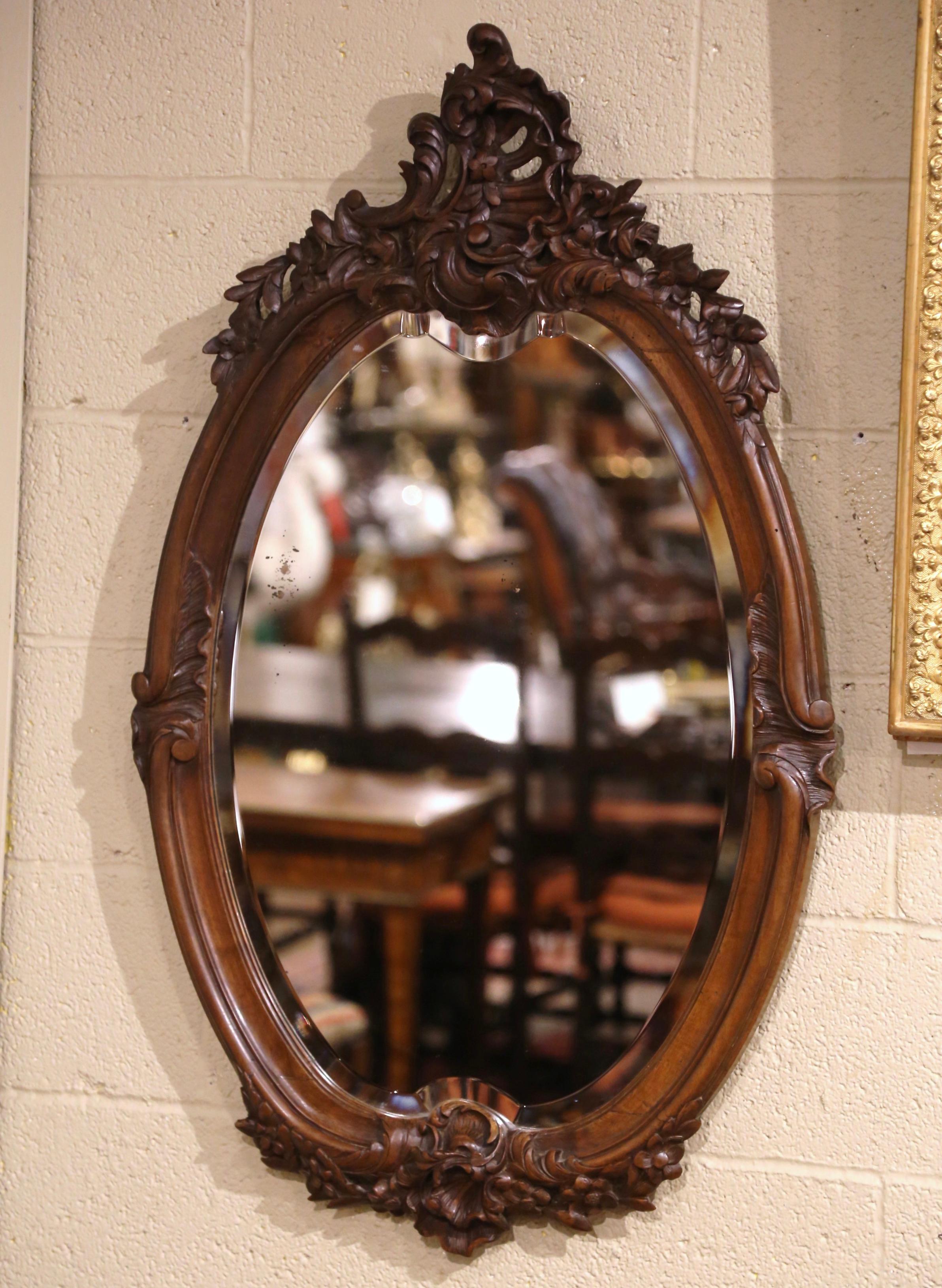 This large antique wall mirror was crafted in France, circa 1870. Oval in shape, the important mirror features hand carved motifs including a large hand carved and pieced cartouche shell motif at the pediment, embellished with foliage, floral decor
