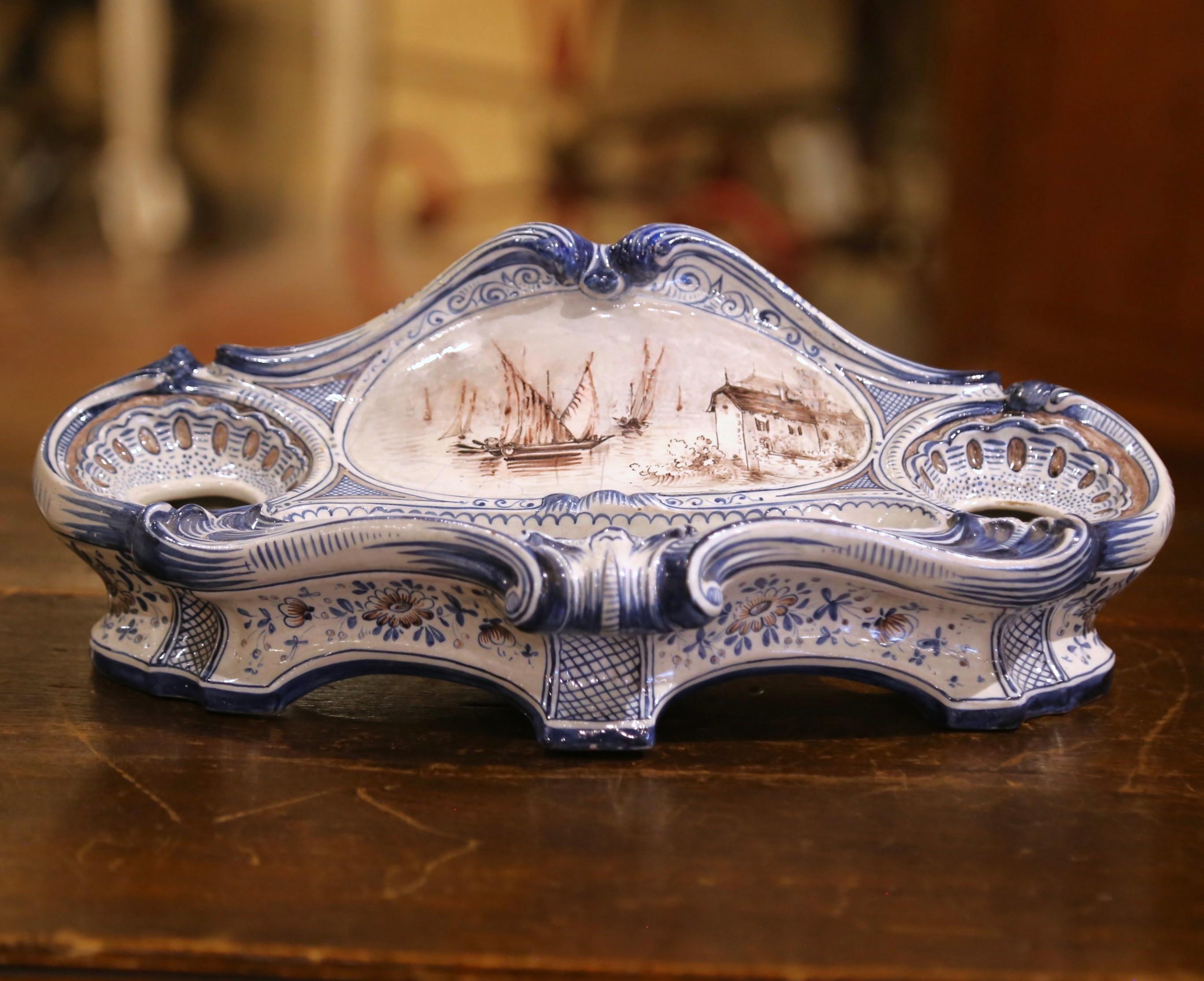 Questo calamaio in ceramica dalla forma unica è stato scolpito in Francia, intorno al 1880. L'essenziale da scrivania a forma di cartiglio presenta un medaglione centrale dipinto a mano in bianco e nero con barche a vela, casali e motivi floreali