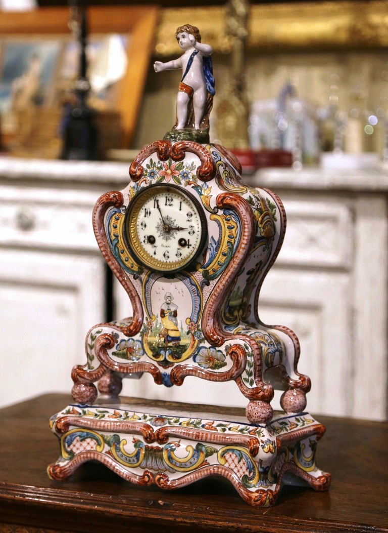 Decorate a mantel or a shelf with this elegant and colorful antique clock. Crafted in Brittany France circa 1890, the ceramic clock stands on an attached base ending with scroll feet, over a bombe front with scalloped apron. The top is decorated