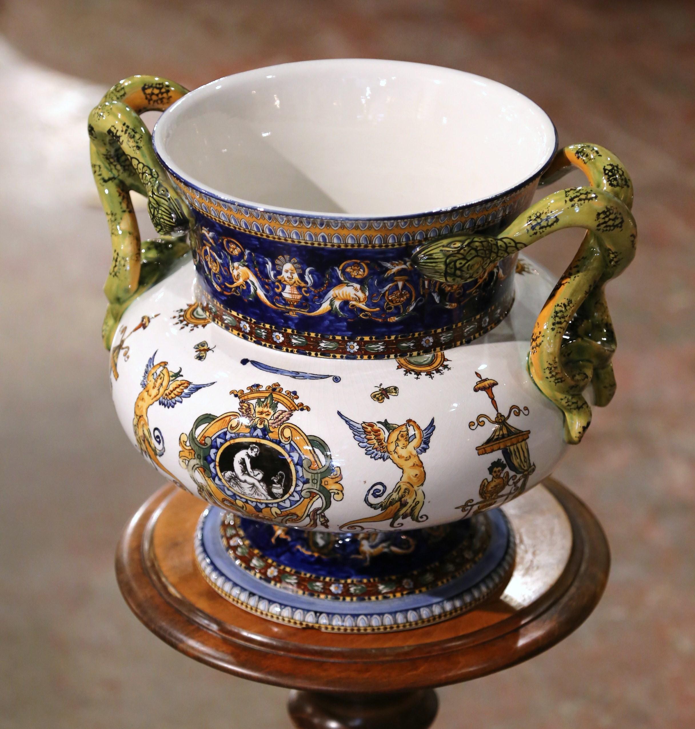 Created in France circa 1890 by the Gien factory, the antique planter is round in shape and stands on a circular base decorated with acanthus leaf motifs. The large cache pot features two twisted snake handles over the colorful rim and wide neck.