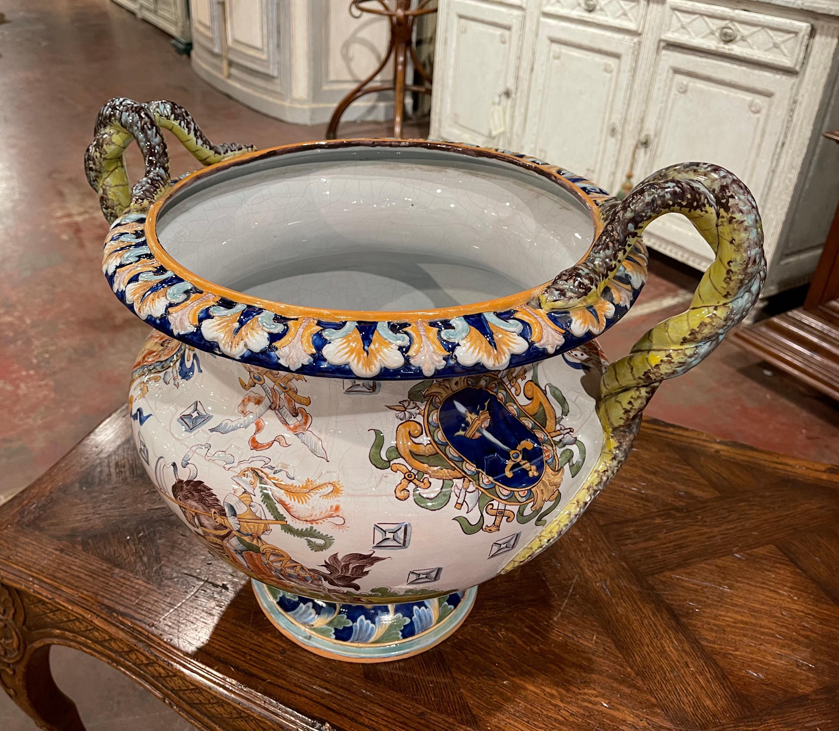 Created in France circa 1890 and attributed to Gien, the antique planter is round in shape and stands on a circular base decorated with acanthus leaf motifs. The large cache pot features two twisted snake handles over the colorful rim and wide neck.