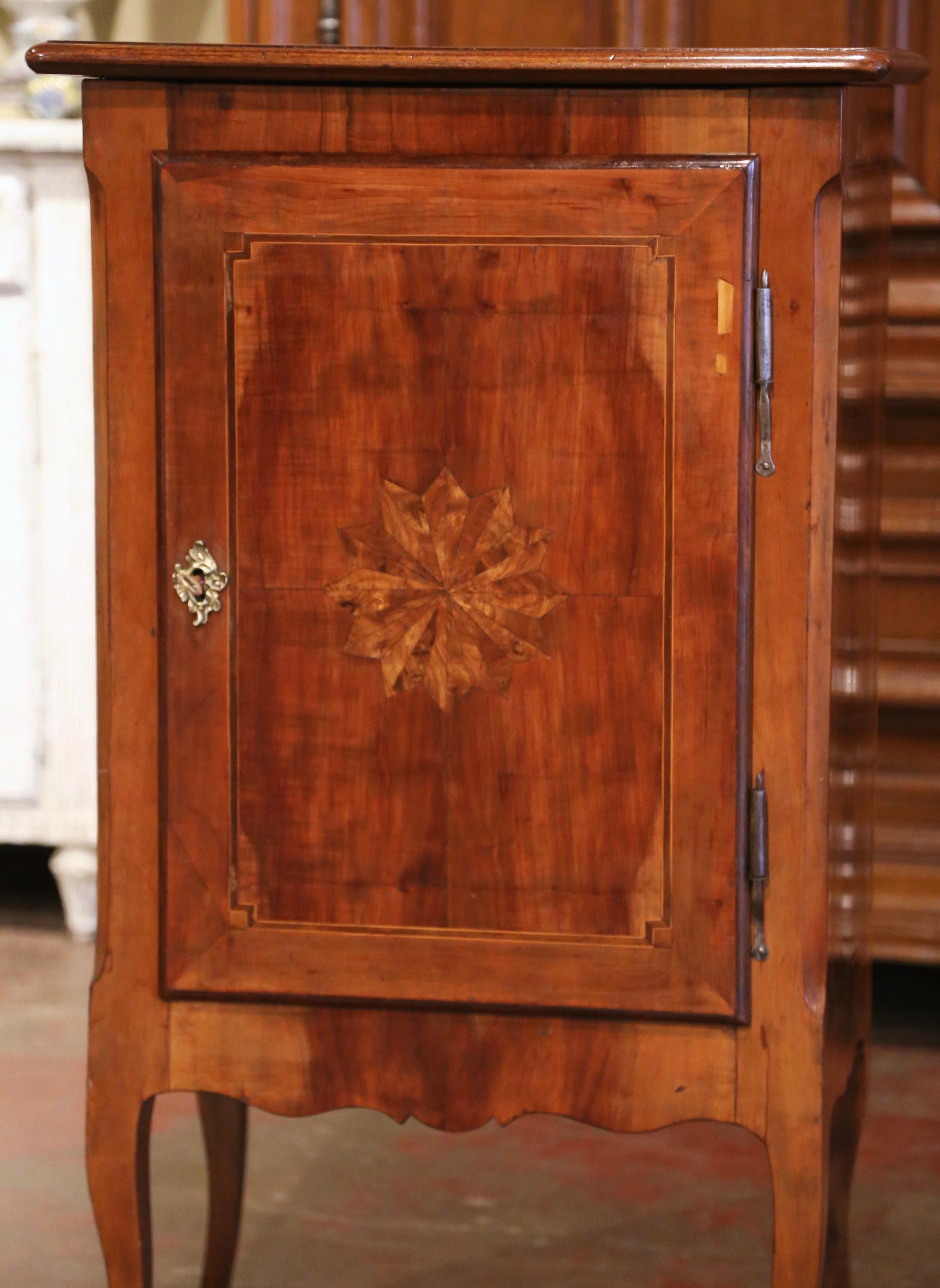 Crafted in Paris, France circa 1880, the antique cabinet stands on cabriole legs ending with bronze sabots over a scalloped apron. The rectangular top with inlaid motifs sits over a single door decorated with contrasting string inlay, and further