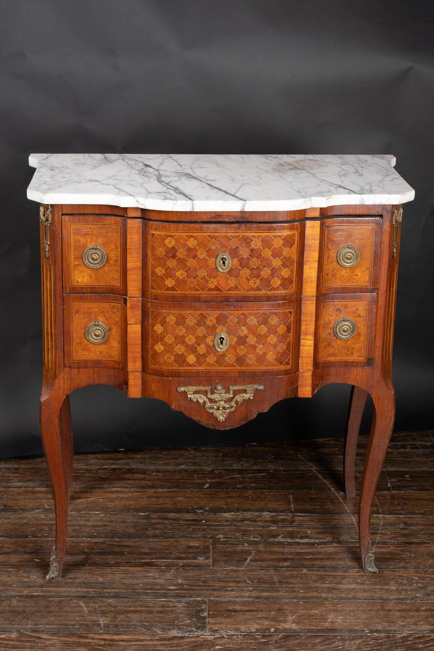 This classic French transition marble top chest with drawers features satinwood, kingwood, is inlaid with burl walnut, and sports detailed marquetry alongside bronze mounts and a marble top. The piece features a body classic to the Louis XVI style,