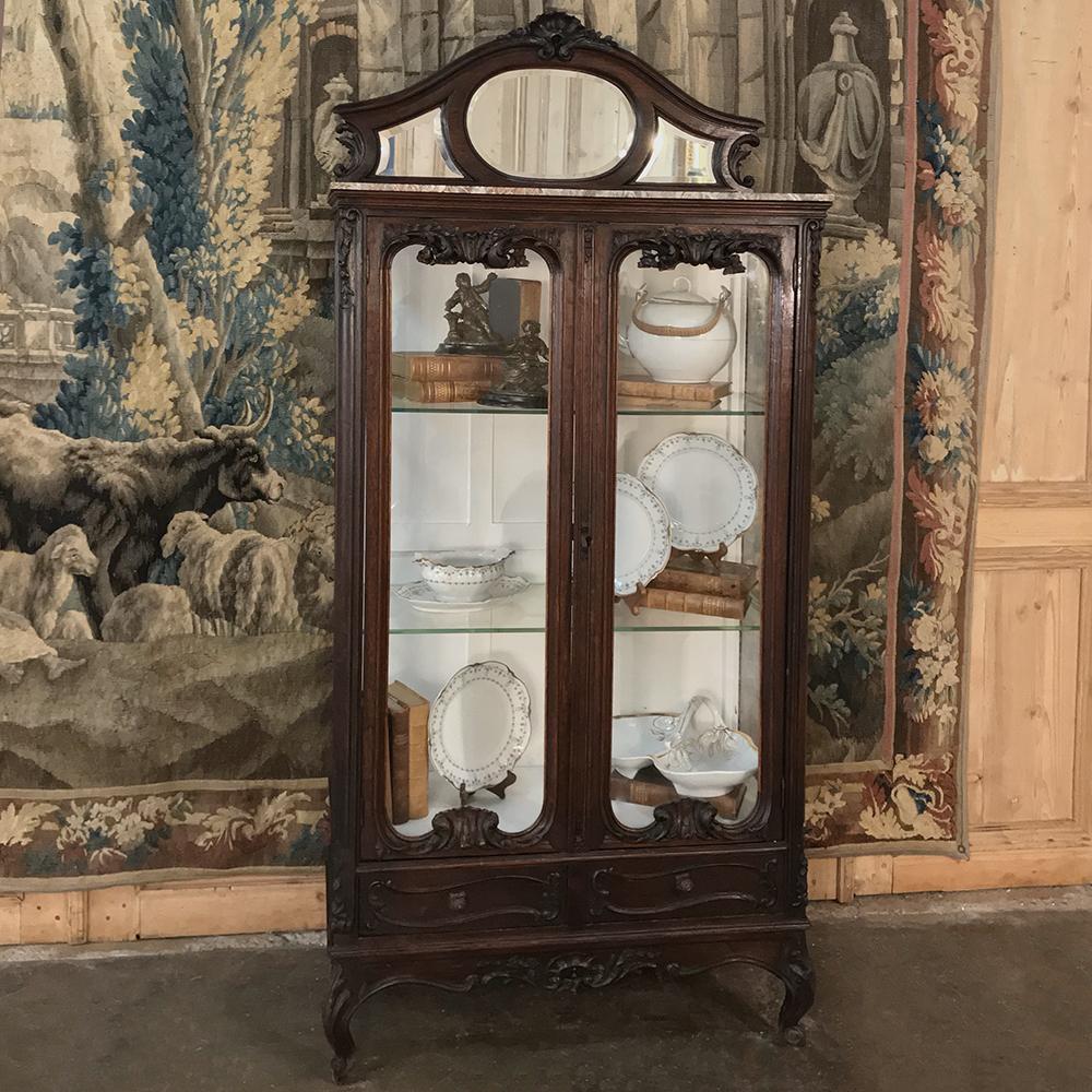 19th century French Louis XV marble top vitrine is a study in the style, with graceful French scrolls adorned with hand carved naturalistic shell, floral and foliate motifs. With glazing on both doors and on both sides, interior lighting is simply