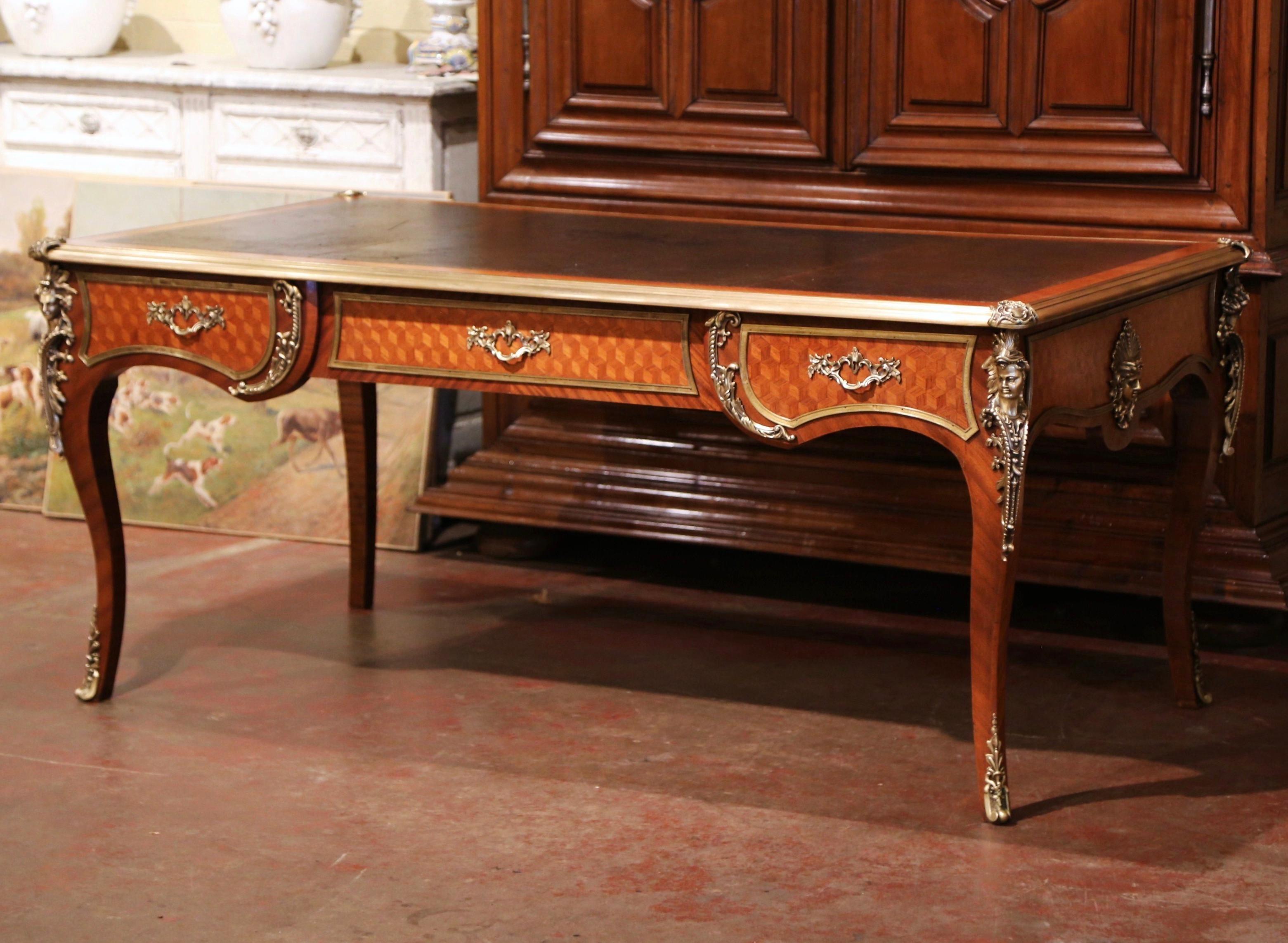 Crafted in Paris, France, circa 1870 in the style of Francois Linke and built of walnut with oak parquetry, the large antique desk stands on elegant cabriole legs decorated at the shoulder with bronze figural busts of woman wearing floral