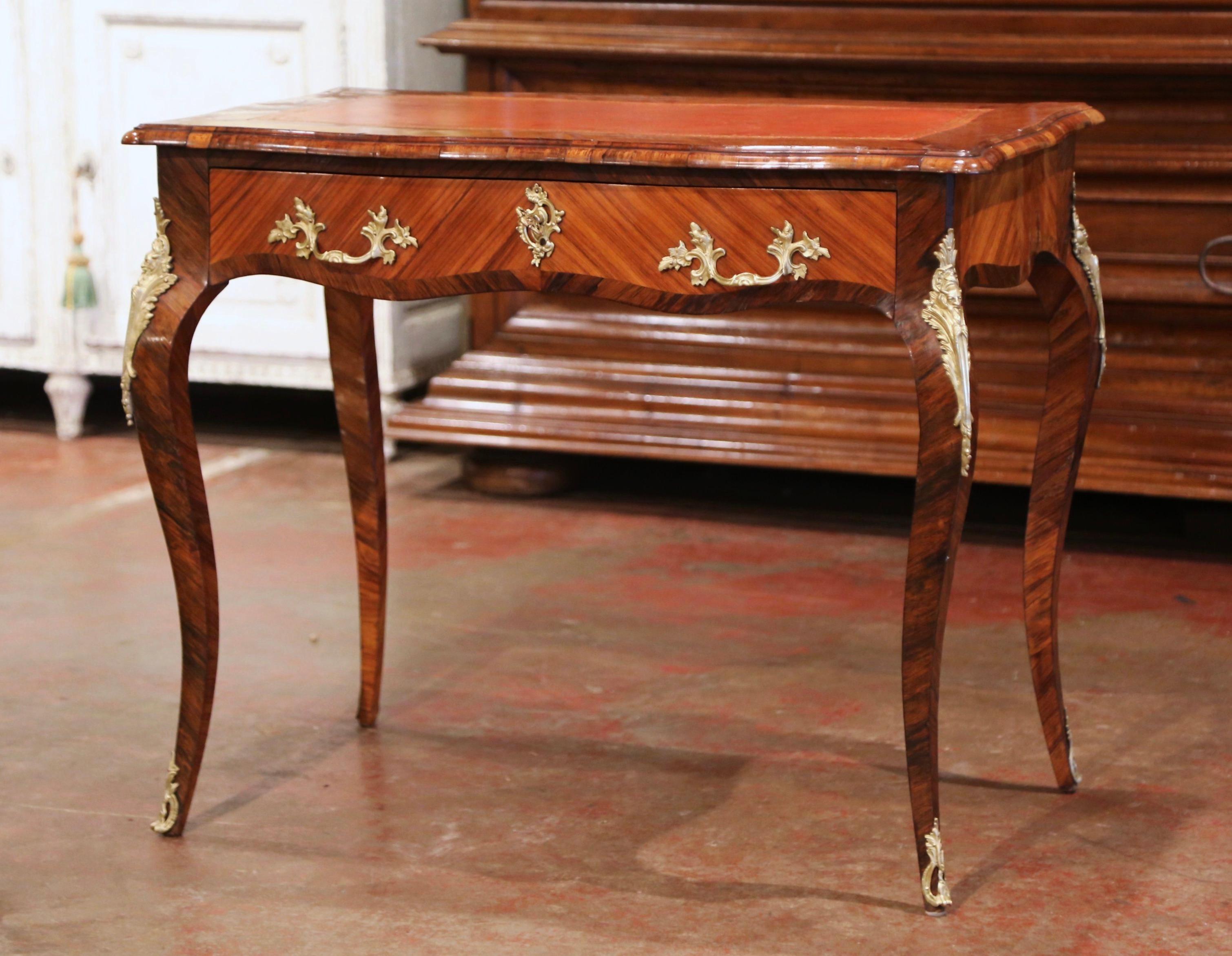 Cette élégante table ancienne en bois de rose a été fabriquée en France, vers 1860. La table à écrire, à la façade serpentine et aux côtés en bombe, repose sur des pieds cabriole habillés de montures en bronze doré aux épaules, et se terminant par