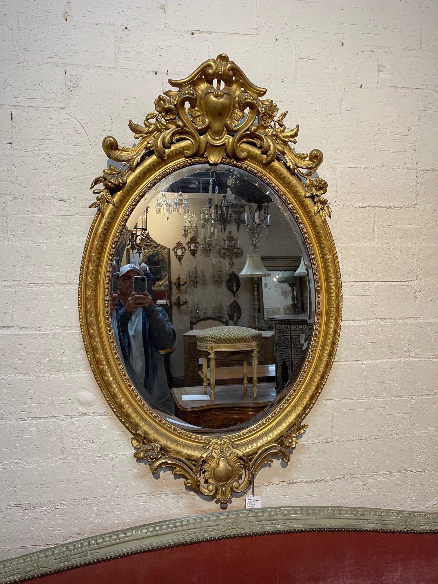 Elegant miroir ovale en bois doré Louis XV du 19ème siècle. Magnifiques sculptures avec des images florales et des écussons. Charmant !