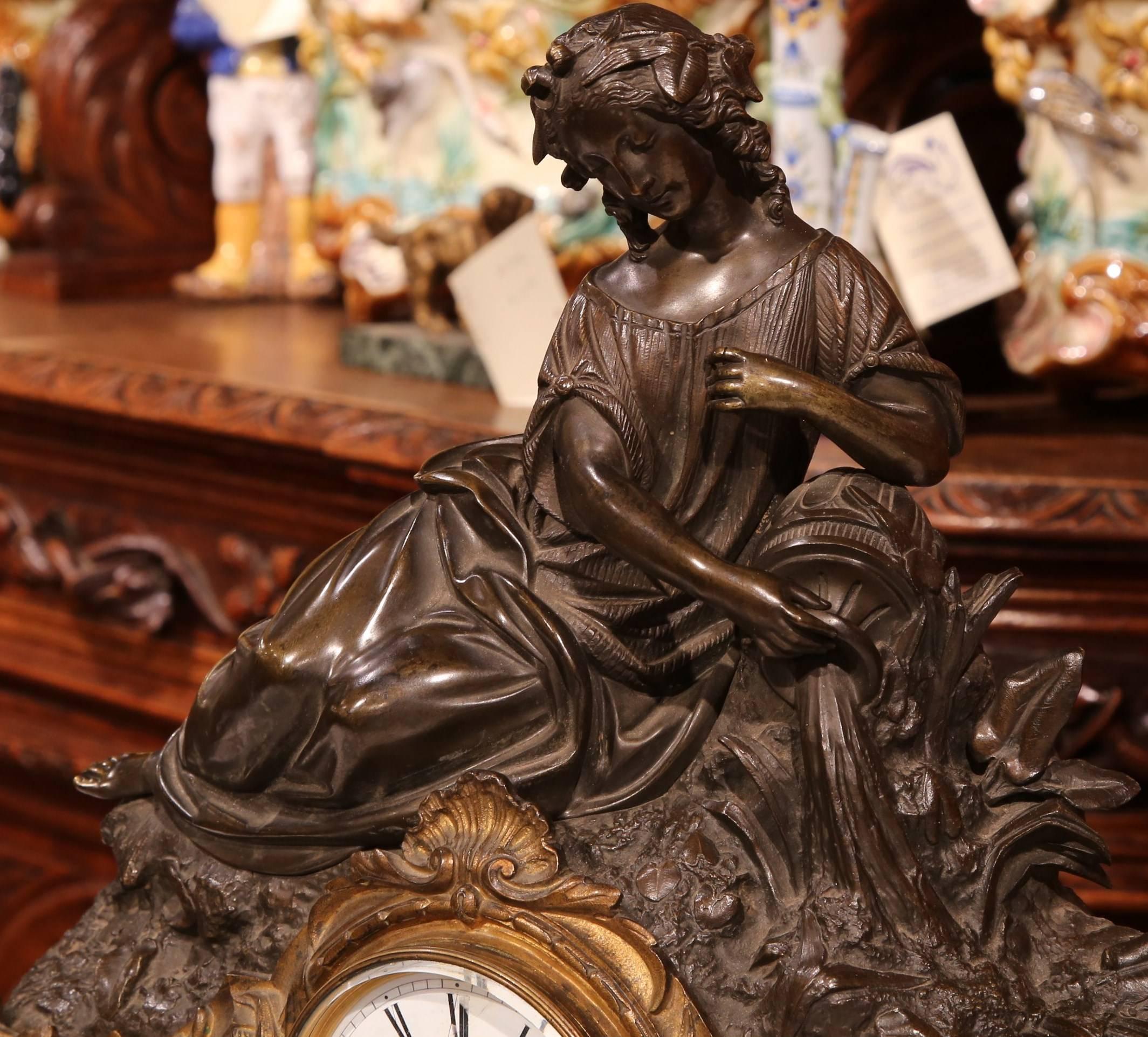 This elegant, two-tone patinated and bronze doré mantel clock was crafted in France, circa 1820. The antique clock stands on scroll feet, and features a Classic, bronze sculpture at the pediment with a young beauty lying down pouring olive oil from