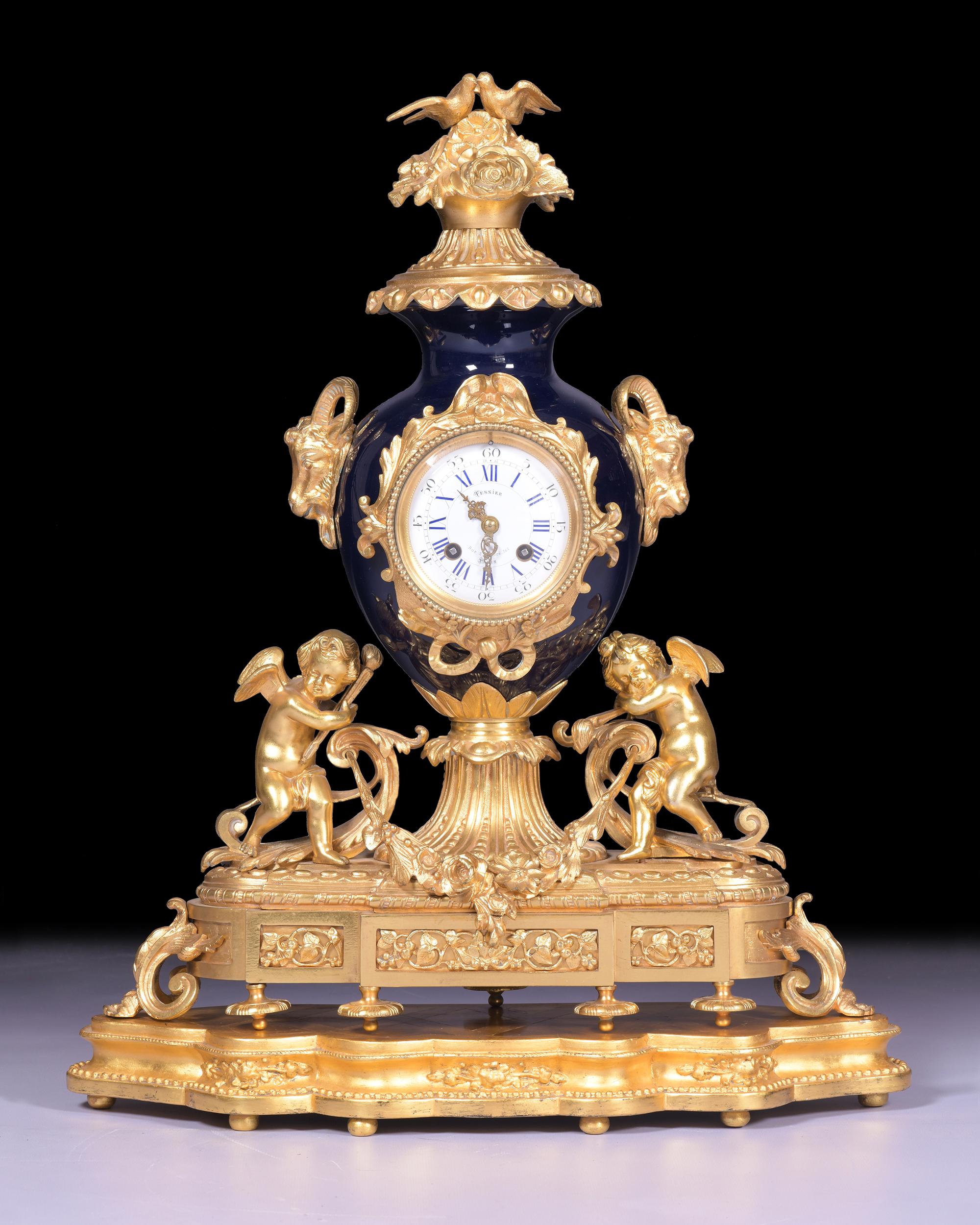 A very fine and most attractive 19th century French Louis XV Rococo Style ormolu and porcelain mantle clock, modelled as an urn with floral finial and goat head masks to the sides, on a plinth base with a pair of figures, the white enamelled dial