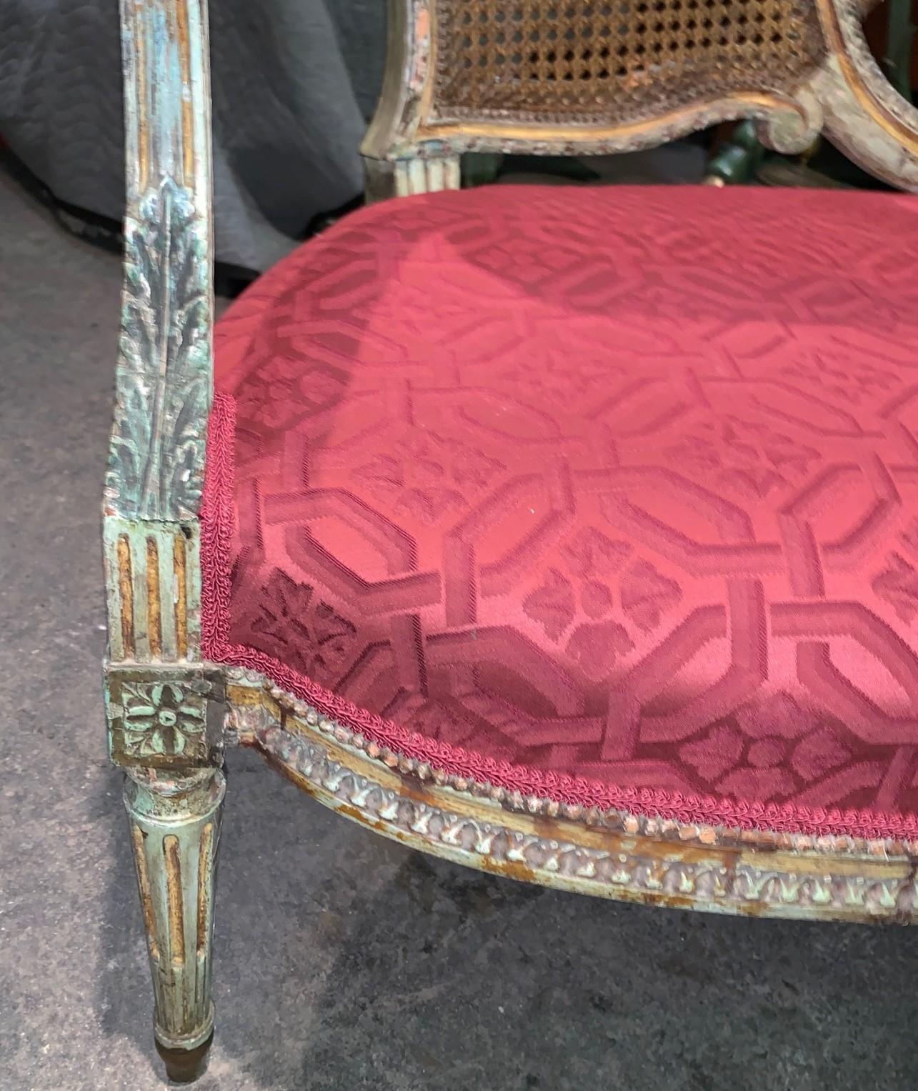 Uniquely styled French Louis XV design painted and caned settee or loveseat. The back superbly carved and ploychromed featuring a quiver of arrows and bow held by a floral motif knotted ribbon. The arms and trim carved with acanthus leaves and