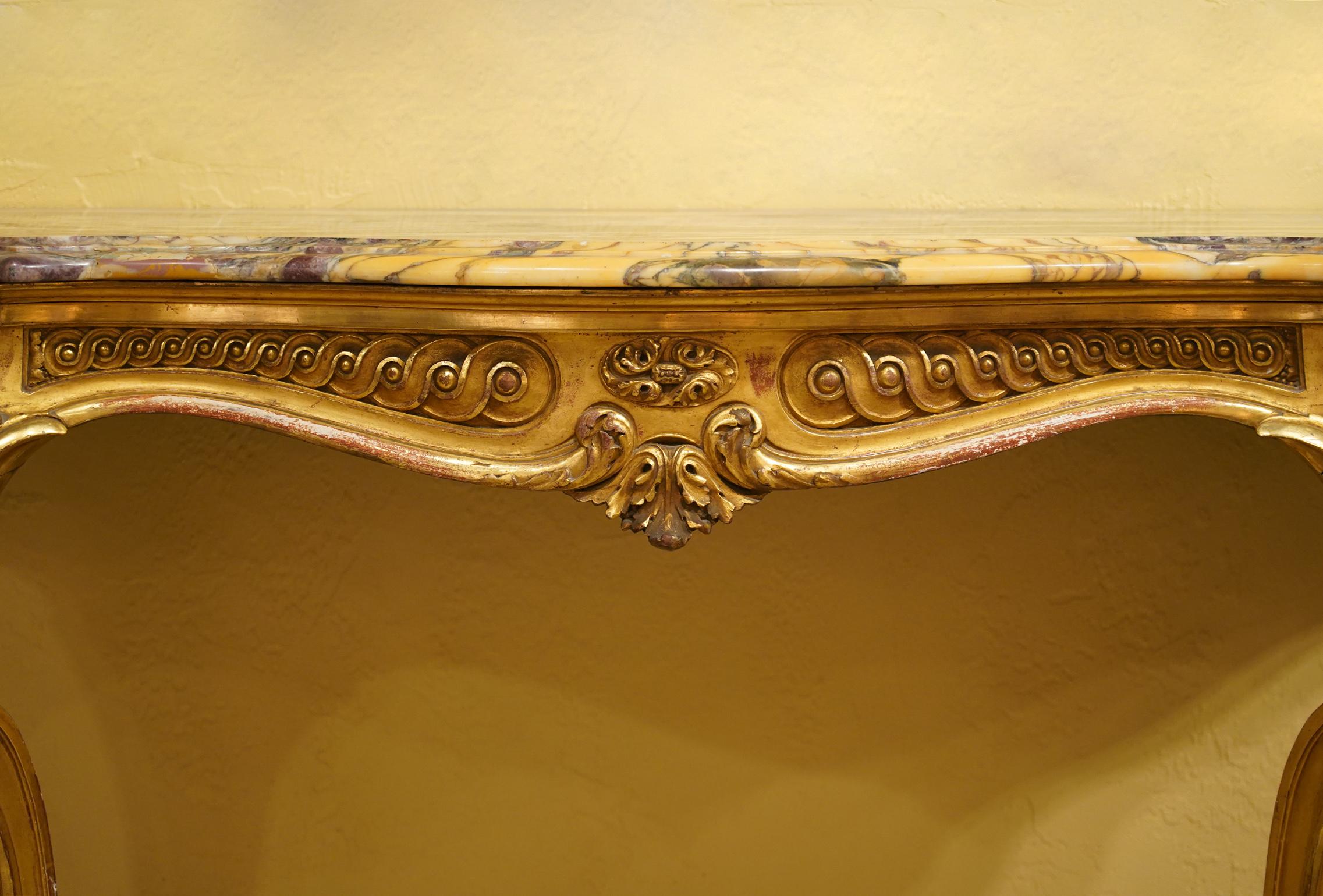 This French Louis XV style console table features a shaped marble top above a serpentine shaped frieze with classical ornaments resting on carved cabriole style legs connected by united stretchers centering a leaf carved finial. A magnificent piece.