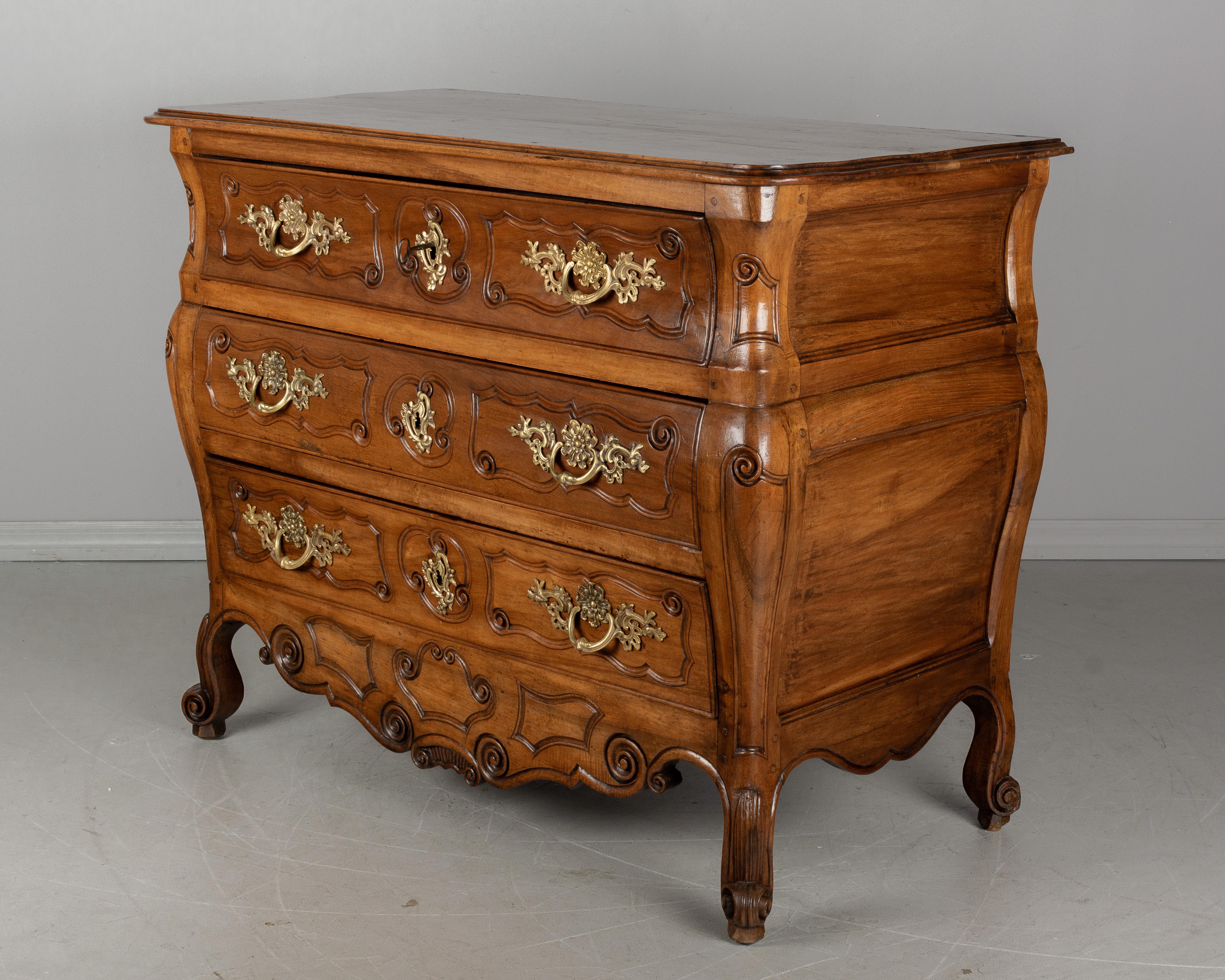 A 19th century French Louis XV style commode, or chest of drawers, from the Bordeaux region made of solid walnut. Large in scale with nice proportions and bombé form. Three dovetailed drawers with carved details and original bronze hardware. Locks