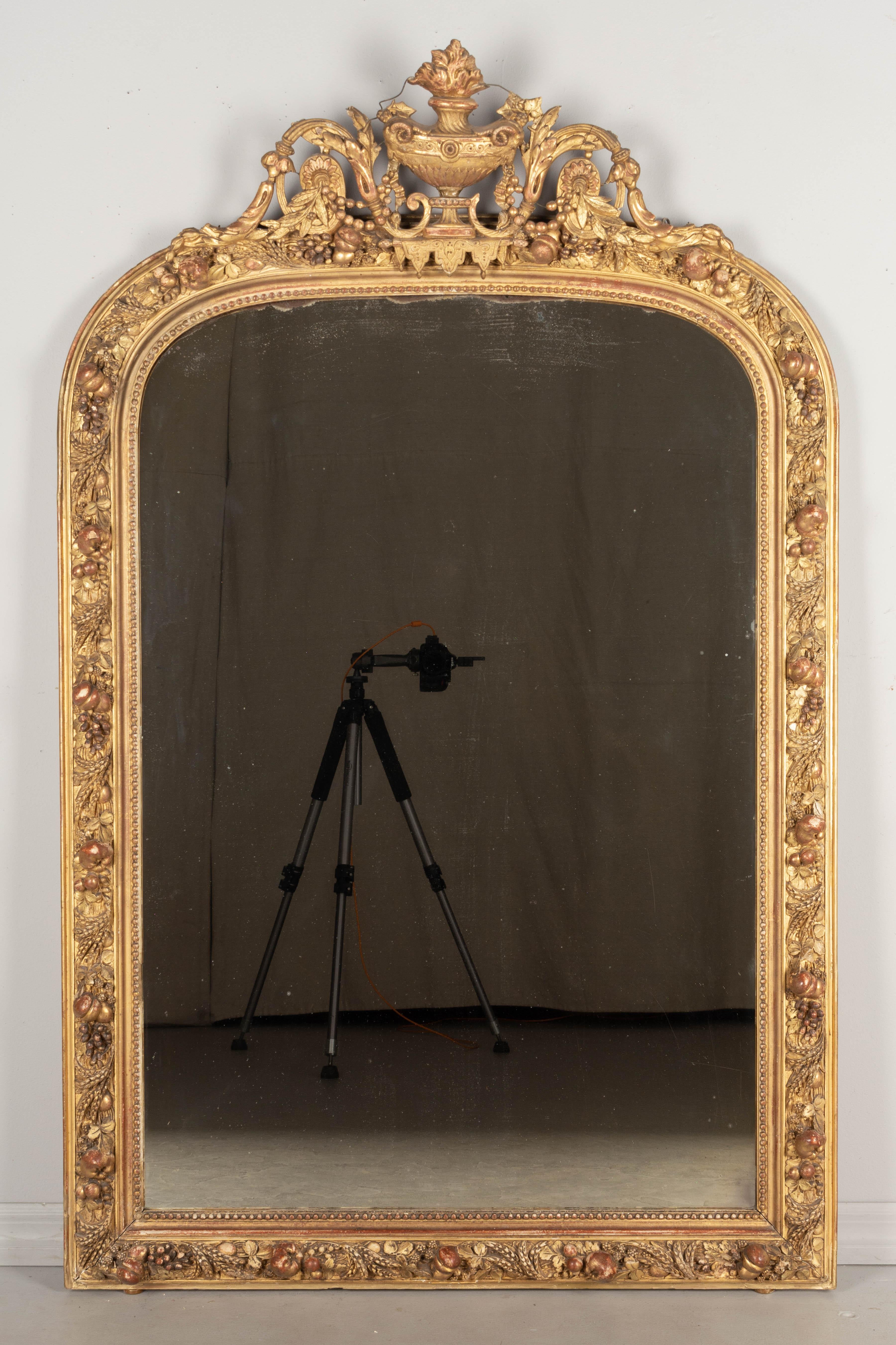 A 19th century Louis XV style gilded mirror with gesso fruits an an elaborate sculptural crest with urn, acanthus leaves, grape clusters and wheat. Nice three dimensional details. Warm gilt finish with some losses and touch-ups. Original mirror with
