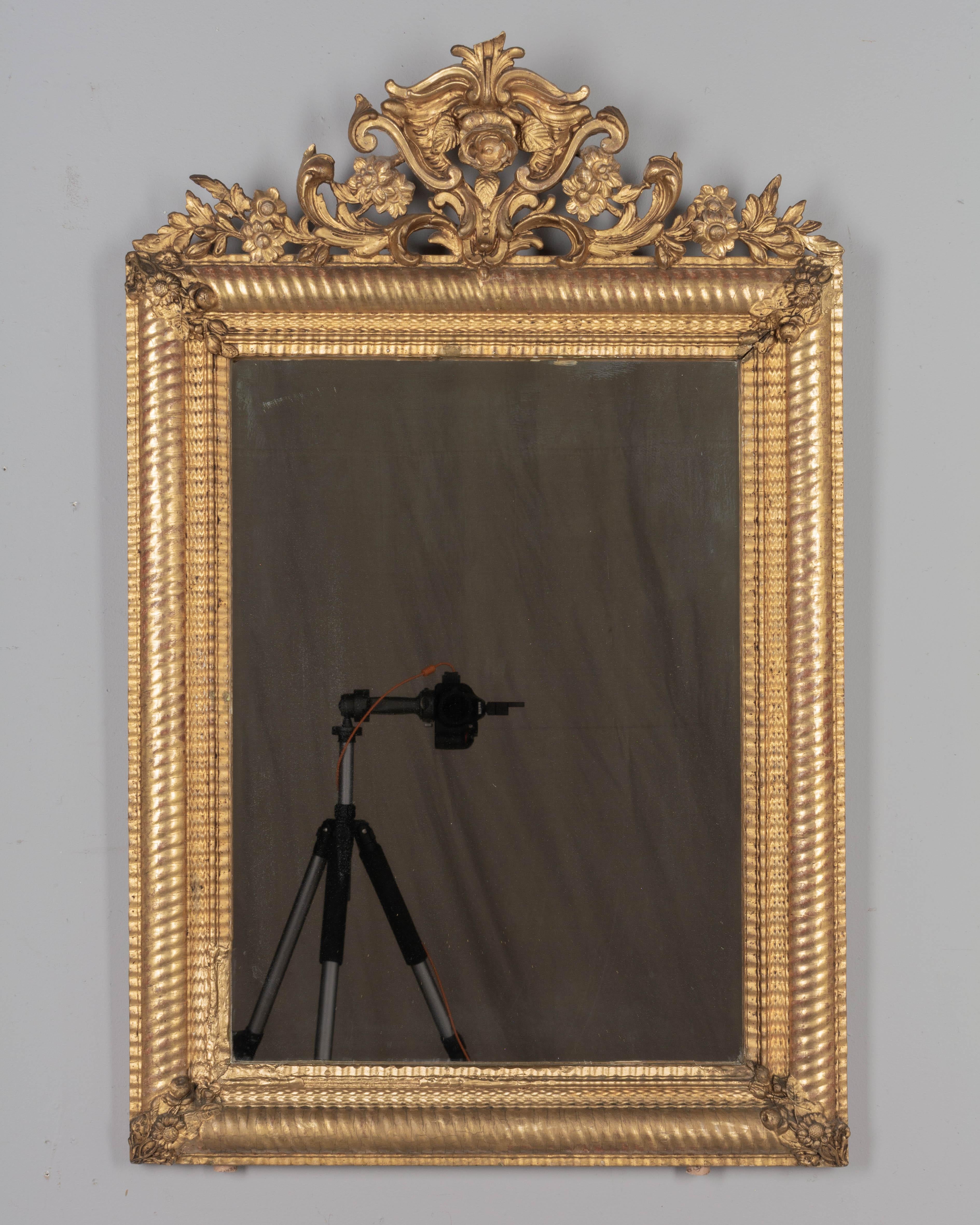 A 19th century Louis XV style gilded mirror with a sculptural floral crest and corner decorations. Nice three dimensional details. Warm gilt finish with some losses and touch-ups. Original mirror. Restorations on the left inner border of frame and