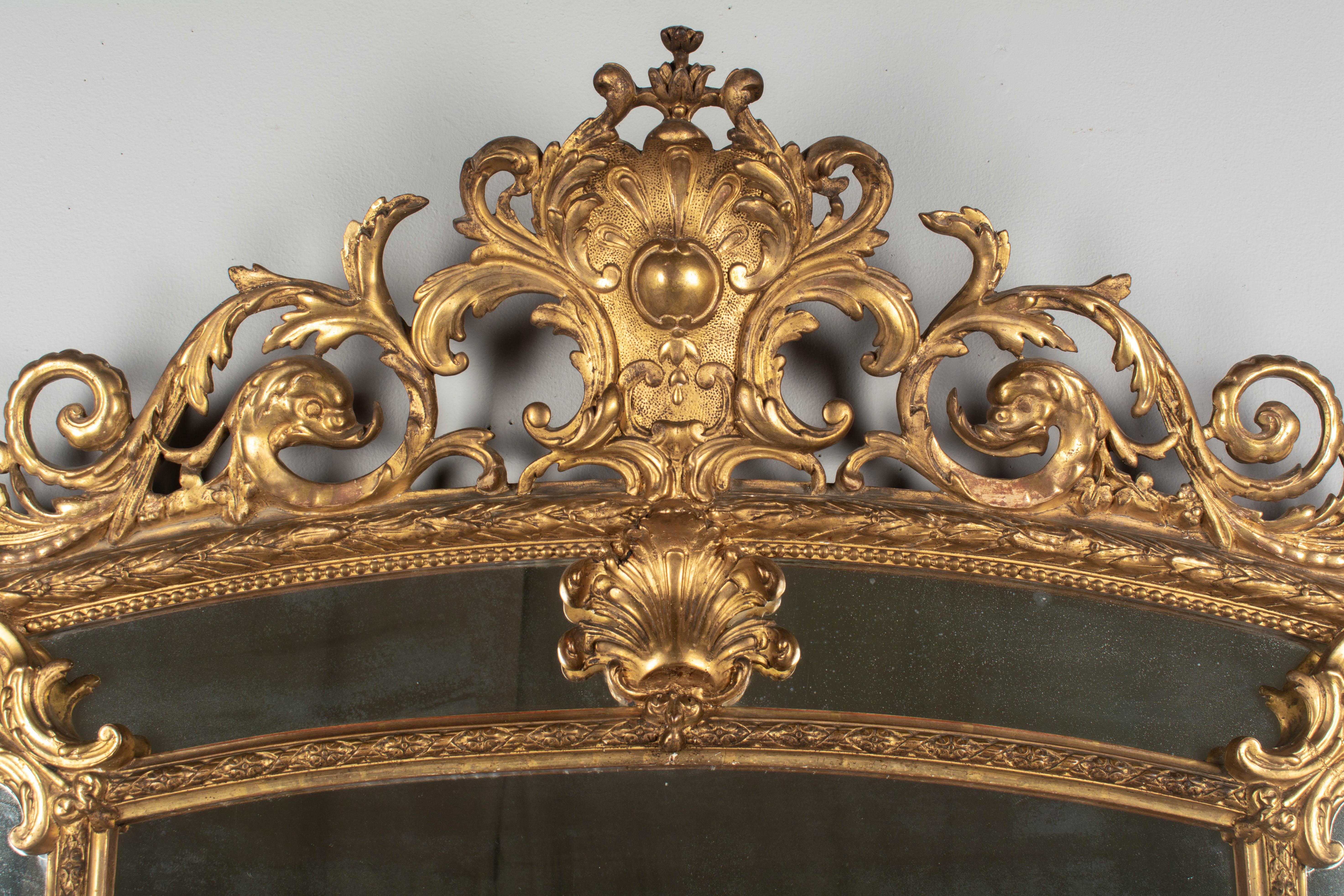 An exceptional Louis XV style giltwood parclose mirror. Elaborate crest with large shell form flanked by dolphins and swirling acanthus leaves. Beautiful carved details include Fleur de Lis motifs in the corners and small flower bouquets on the
