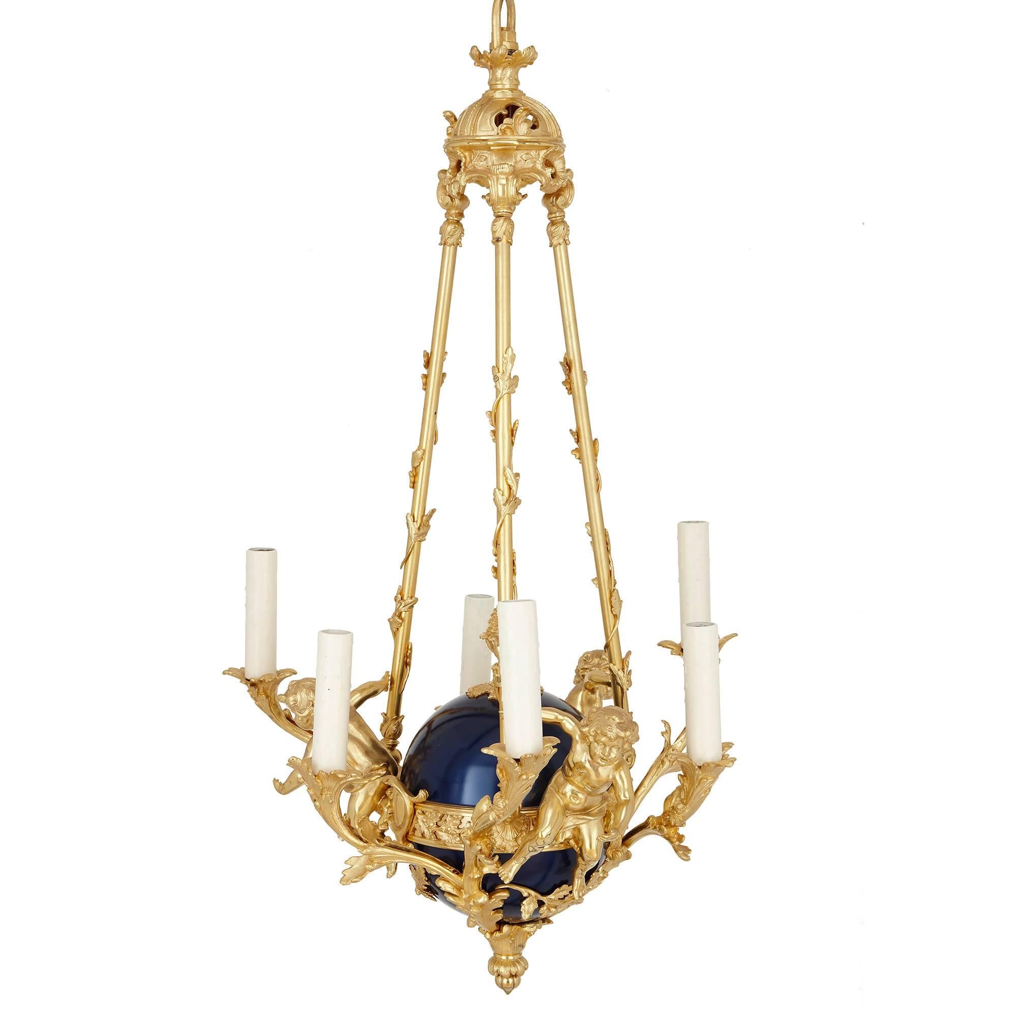 This charming chandelier is crafted in ormolu and tole. The chandelier hangs from an ormolu crown-form support which features rocaille motifs and acanthus leaf form decorations. From the crown extend three ormolu poles, which are entwined with
