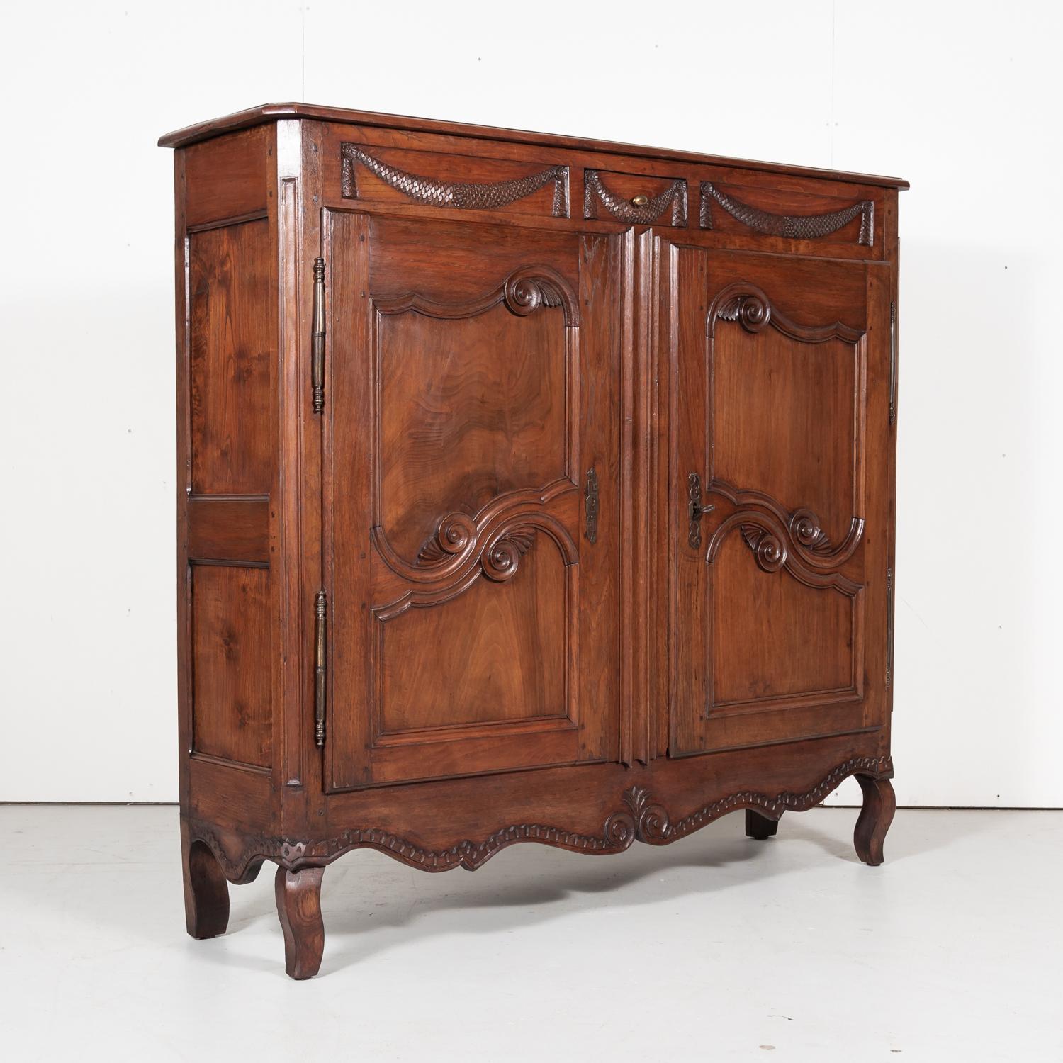 Antique French Louis XV style Provençal bassette or small armoire handcrafted near Avignon of cherry wood, circa 1850s. This provincial piece features intricately carved fish scale swags, S-scrolls, and stylized plumes. The raised and recessed