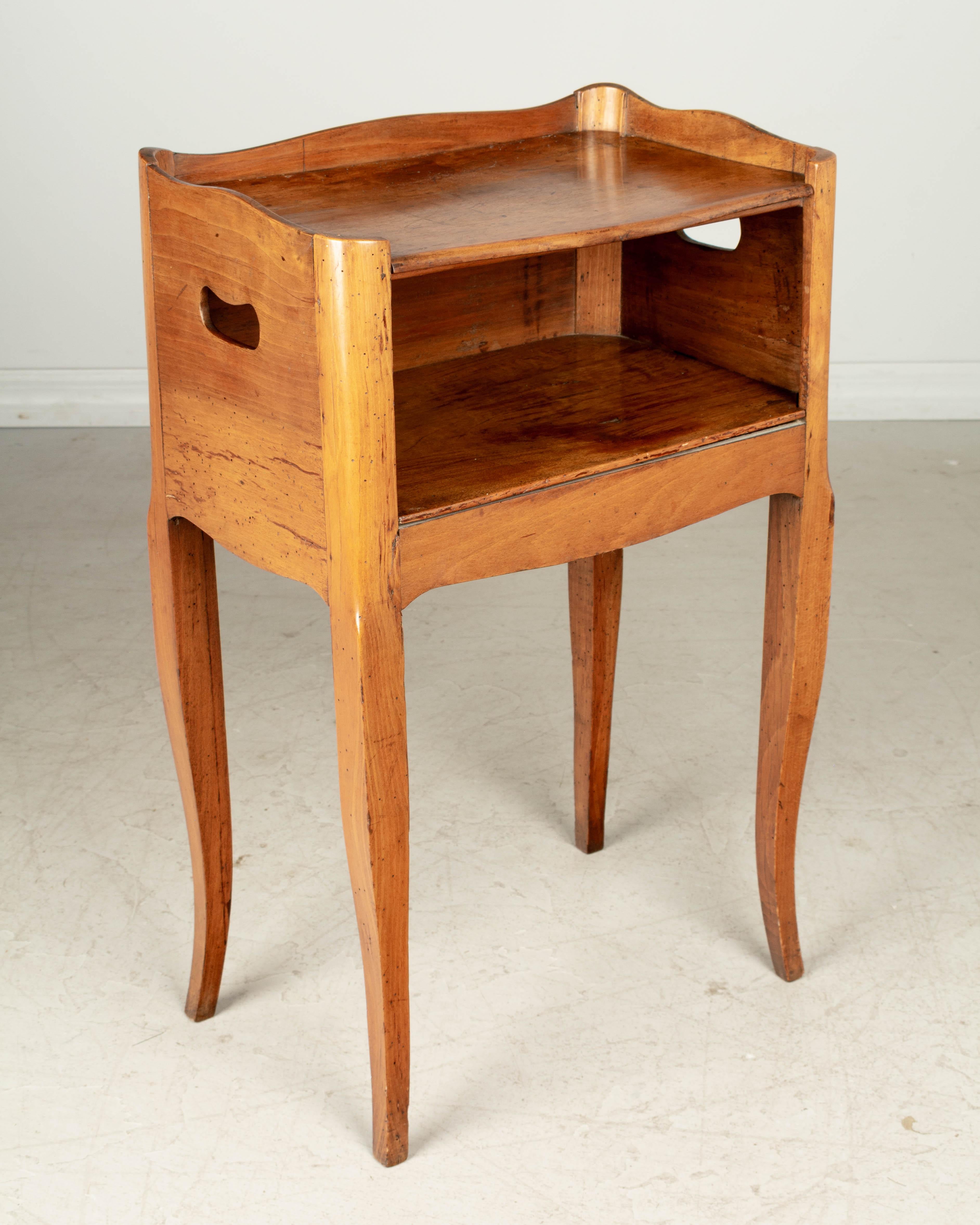 A Louis XV style Country French side table or nightstand made of solid walnut, with open niche and pierced cut-out handles. Small dovetailed drawer on the right side. Curved front corners, and gallery surrounding the top. Waxed finish. All original.