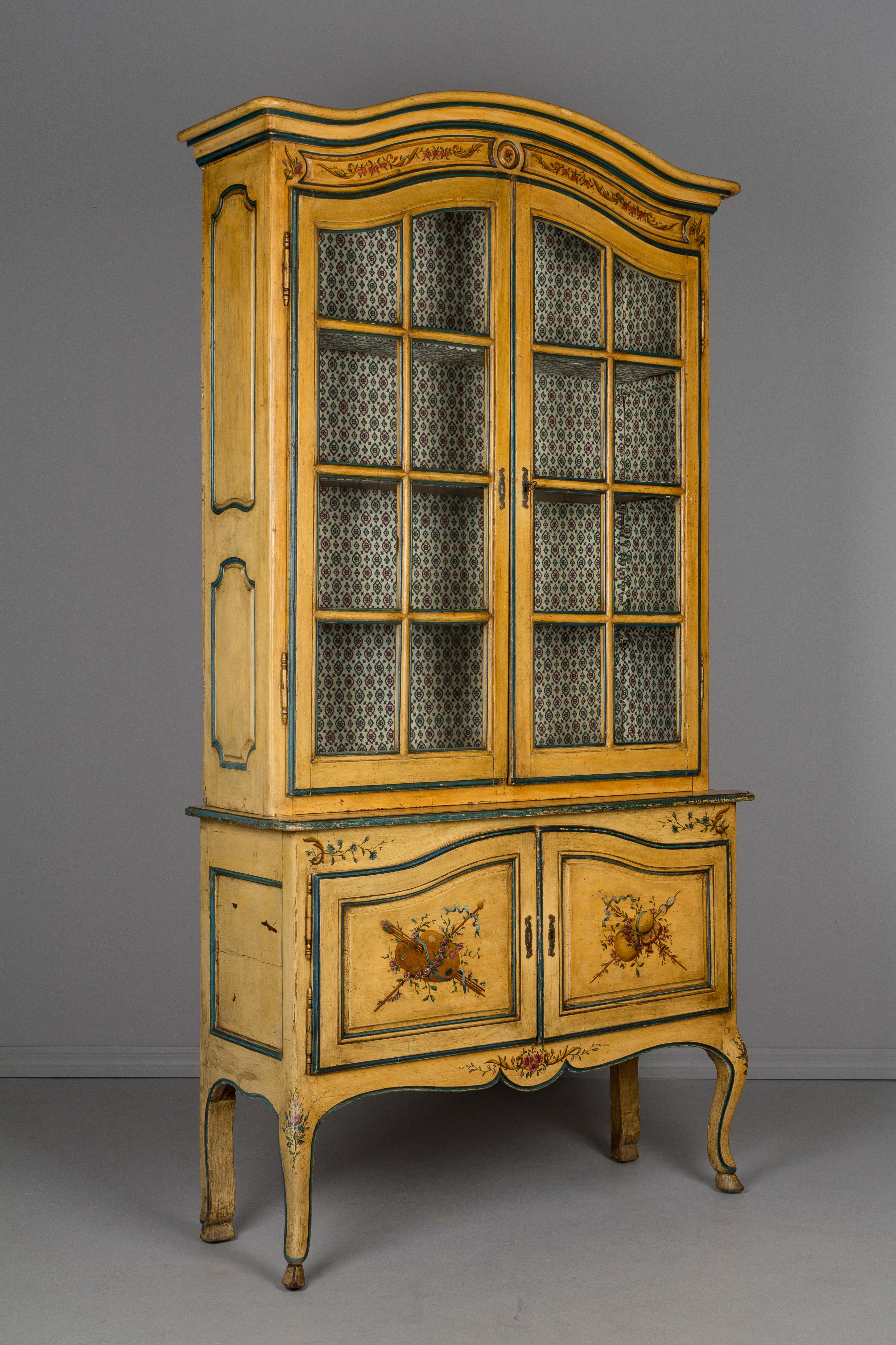 An early 19th century French Louis XV style vitrine, or china cabinet made of pine and oak with pegged construction and painted in the Provençal manner. In two parts, the bottom buffet on curved legs and having two doors with a working lock. The