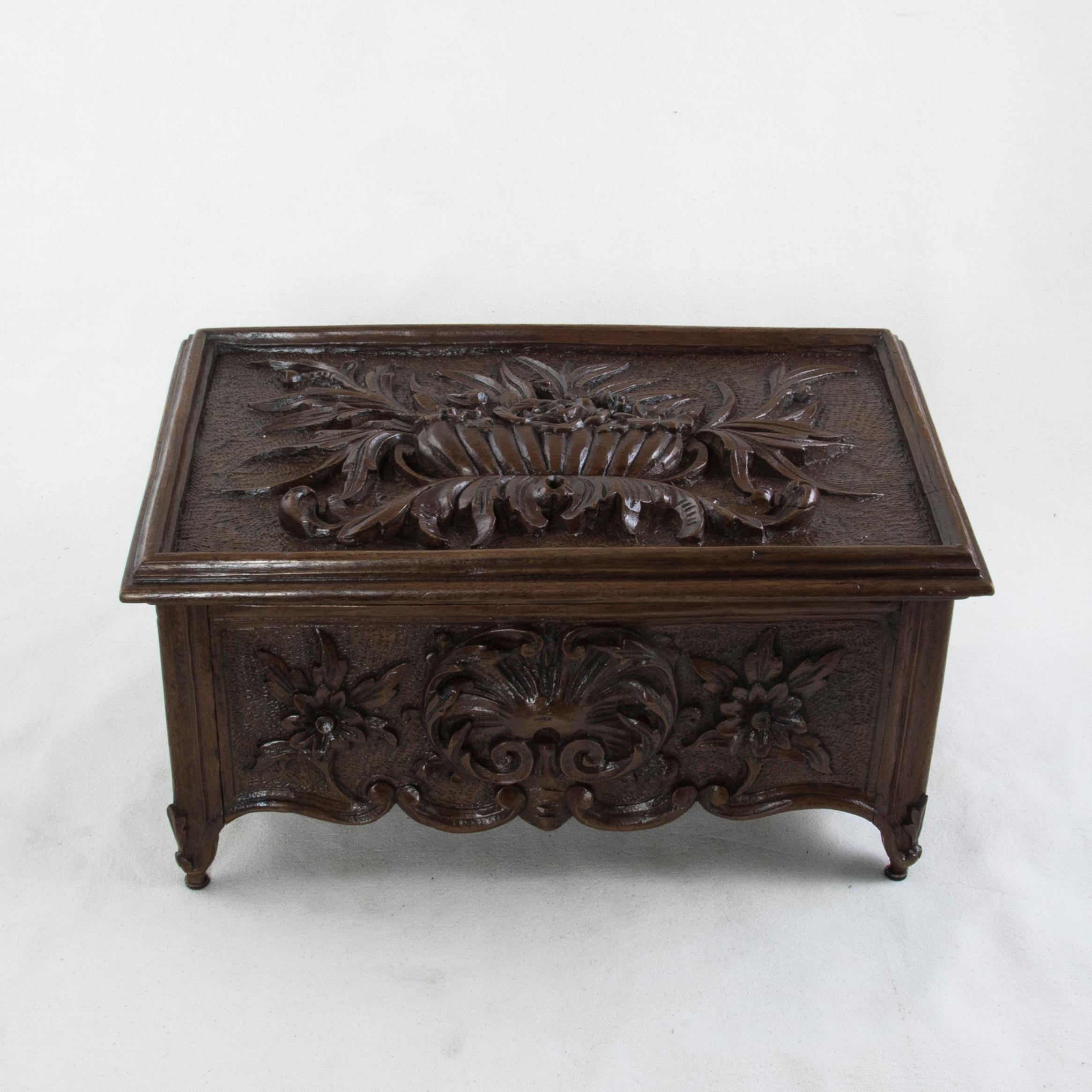 This large late 19th century French Louis XV style walnut box features deep relief hand carved details on all sides. The lid of the box displays a large bouquet of flowers in a basket. The front is detailed with a scrolled shell flanked by flowers