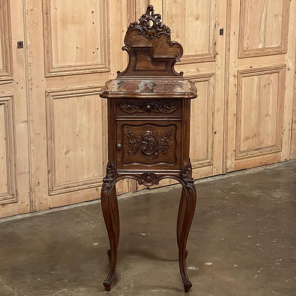19th Century French Louis XV walnut marble top nightstand is a classic example of the genre, rendered in sumptuous French walnut and topped with beautifully veined marble for a timeless effect. The front facade has been masterfully carved directly