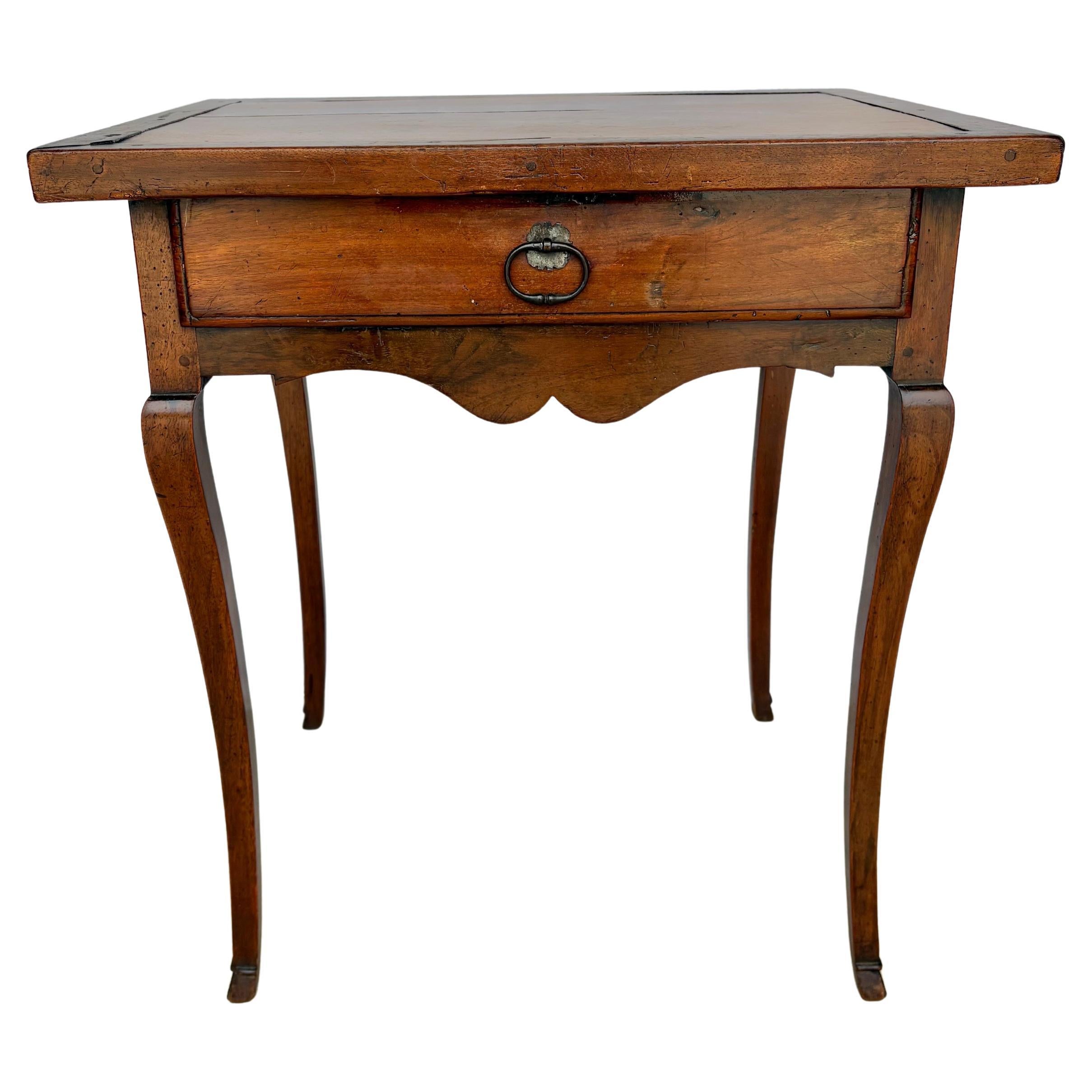 Trouvée dans le sud de la France, cette table d'appoint du XIXe siècle a été fabriquée à la main en noyer ancien par des artisans français dans les années 1800. La pièce présente un dessus à bandeau reposant sur un tiroir à queue d'aronde qui a