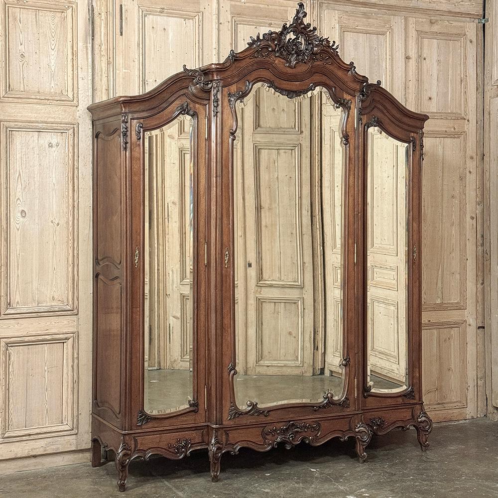19th Century French Louis XV Walnut Triple Armoire is a sublimely stately expression of the refined Rococo style performed by master artisans from sumptous French walnut.  The casework features a center step-front design with three cabinets accessed
