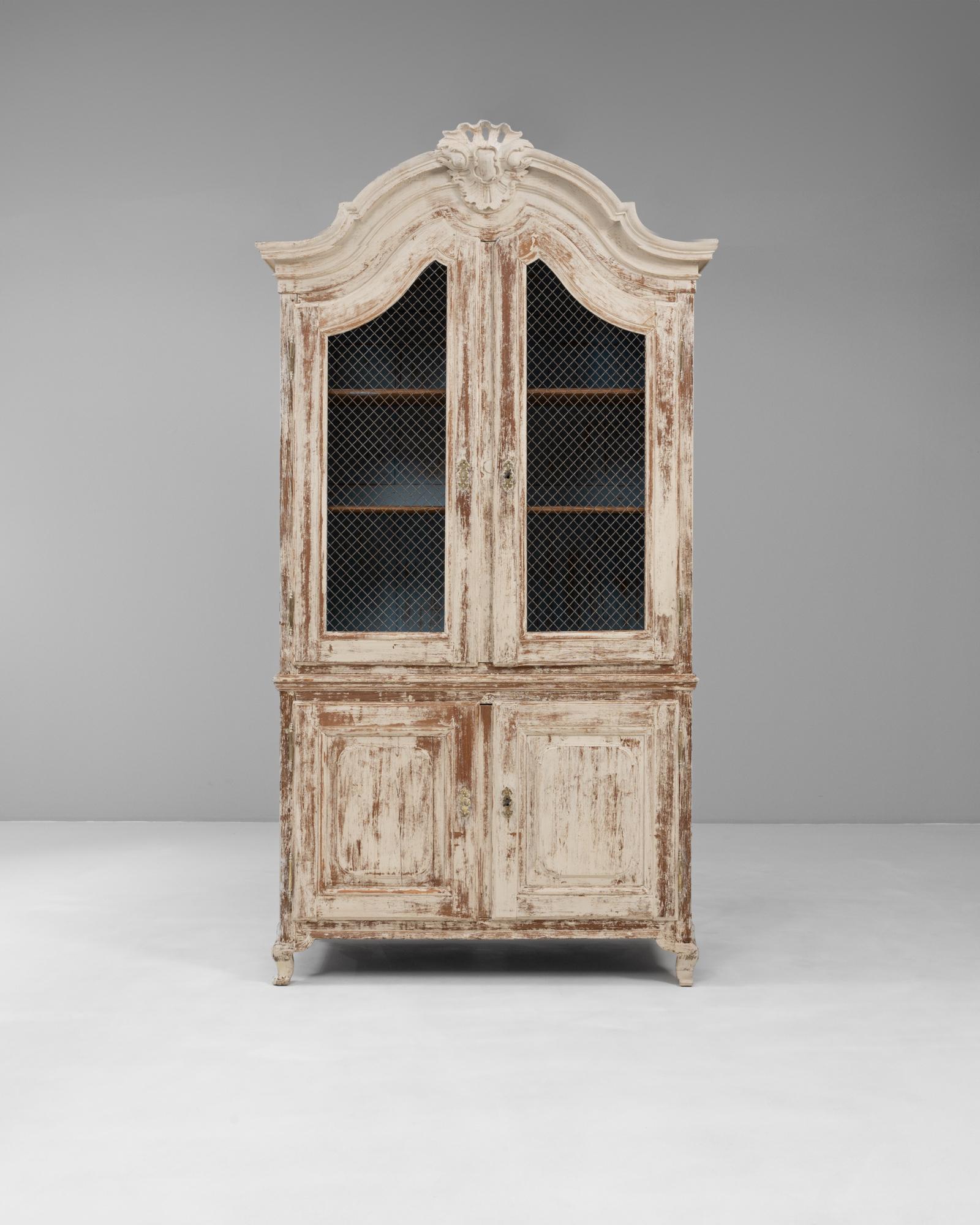 This 19th-century French Louis XV cabinet exudes timeless elegance with its graceful curves and richly patinated finish. Crafted from wood, it features a beautifully carved arched crown adorned with a shell motif, double mesh wire doors, and paneled