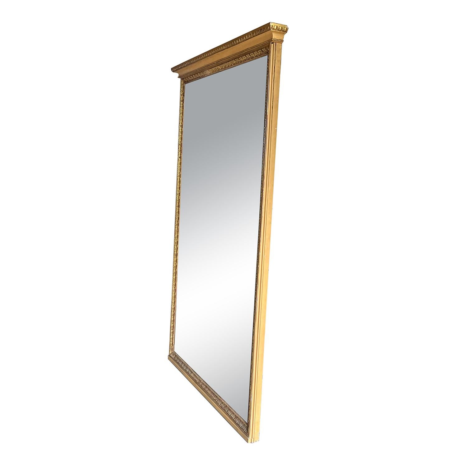 An early 19th Century, antique monumental French Trumeau mirror with its original mirrored glass, made of hand crafted gilded Pinewood in good condition. The full-length floor mirror is particularized with a large top molding and multiple original