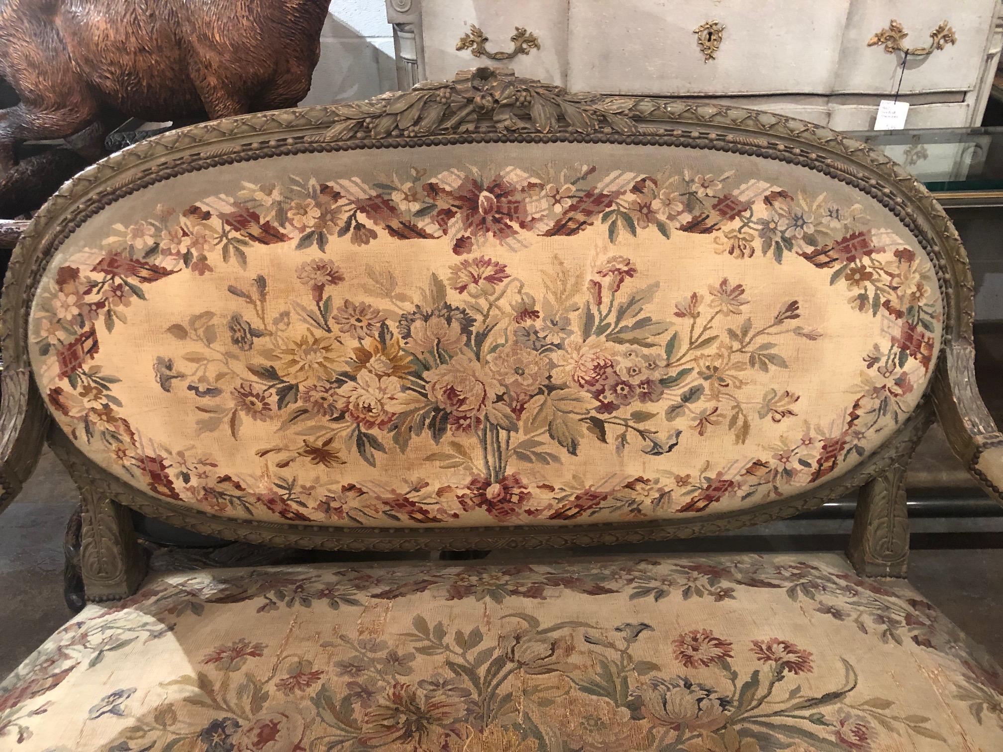 Fabulous 19th century French Louis XVI style settee with grayish painted finish. The crest and skirt superbly with hand-carved leaf clusters and leaf sprays. Upholstered in a beautiful and colorful Aubusson style floral motif tapestry. The entire on