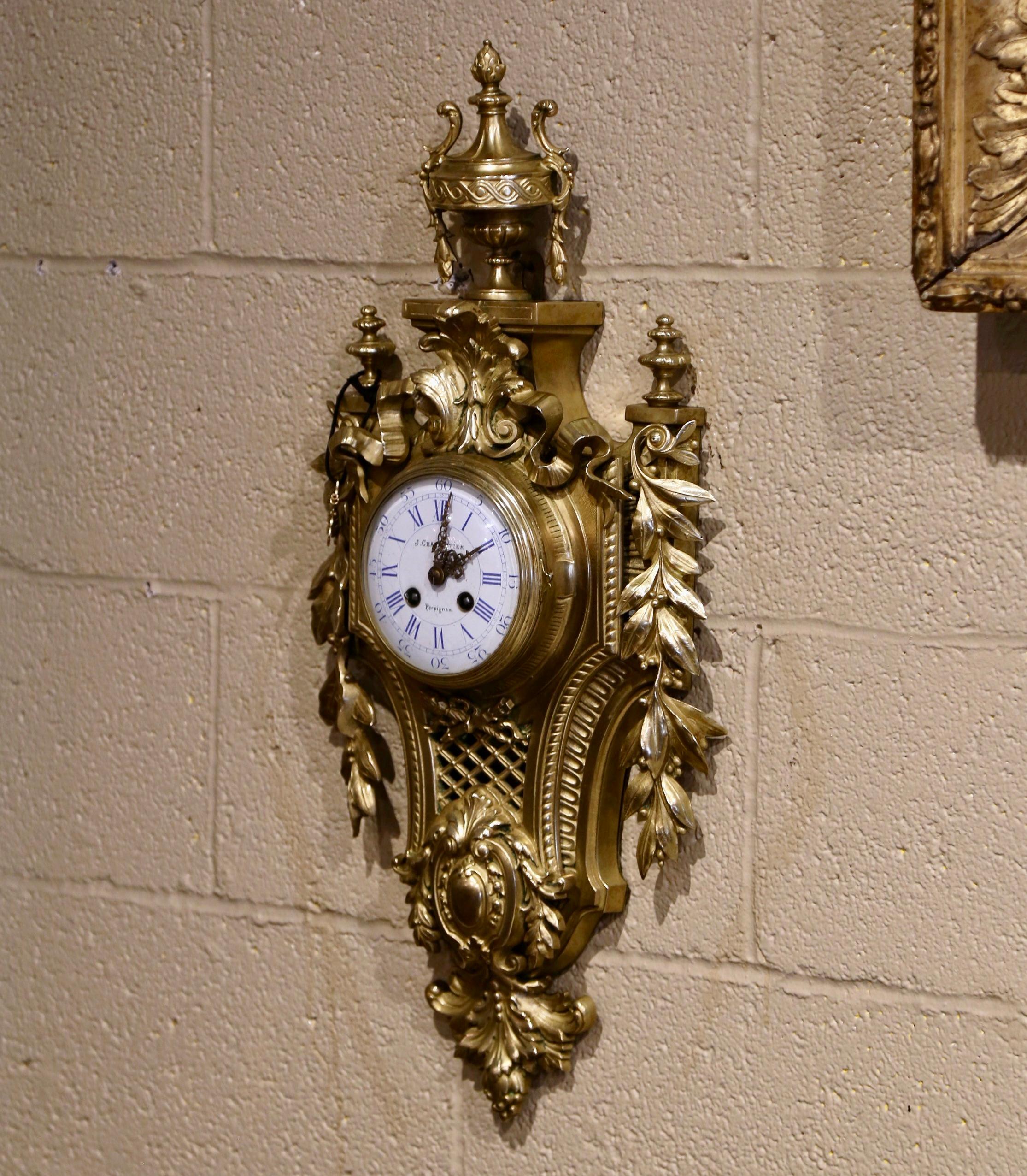Crafted in Perpignan, southwest France, circa 1870, the wall clock made of bronze, features intricate decor in high relief. The pediment has a classic urn shape and the sides are decorated with laurel leaves. The porcelain dial, signed Charpentier,