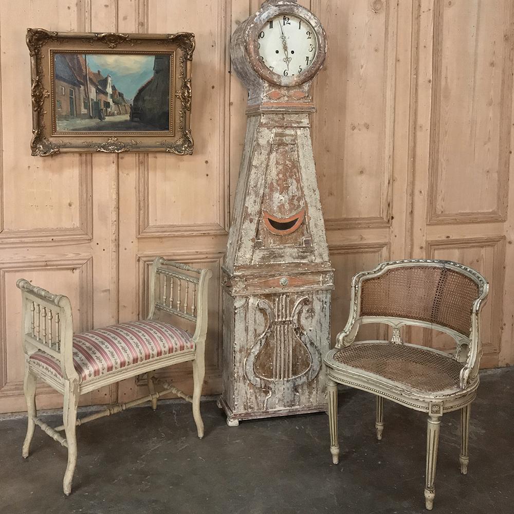 19th century French Louis XVI caned vanity bench features a wonderful distressed painted finish that accentuates the spiral ribbon and acanthus leaf motifs hand-carved into the framework. Caned seatback and seat provide lightweight, airy