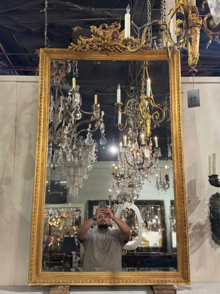 El espejo francés del siglo XIX Luis XVI tallado y dorado es una pieza impresionante  que desprende elegancia y sofisticación. El marco del espejo está meticulosamente tallado y adornado con intrincada madera dorada, lo que le confiere un aspecto