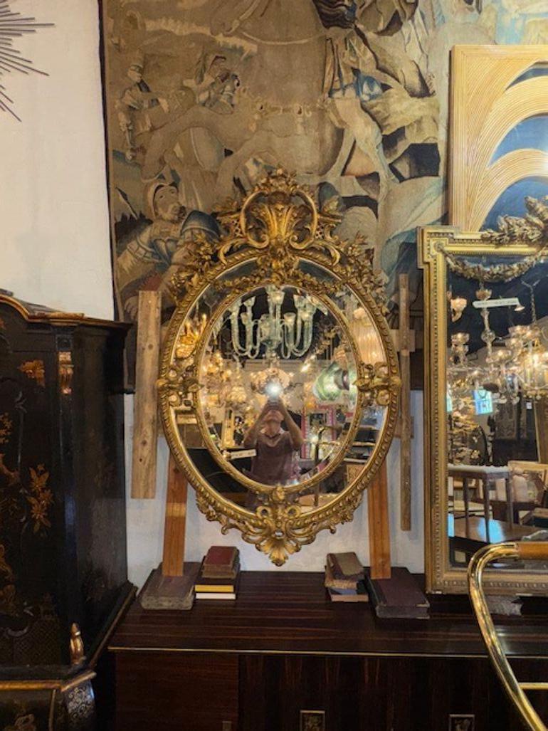 Questo specchio ovale francese del XIX secolo di Eleg XVI è caratterizzato da una splendida cornice in legno dorato e intagliato, che emana eleganza e raffinatezza. Lo specchio è progettato nel classico stile Luigi XVI, noto per i suoi dettagli