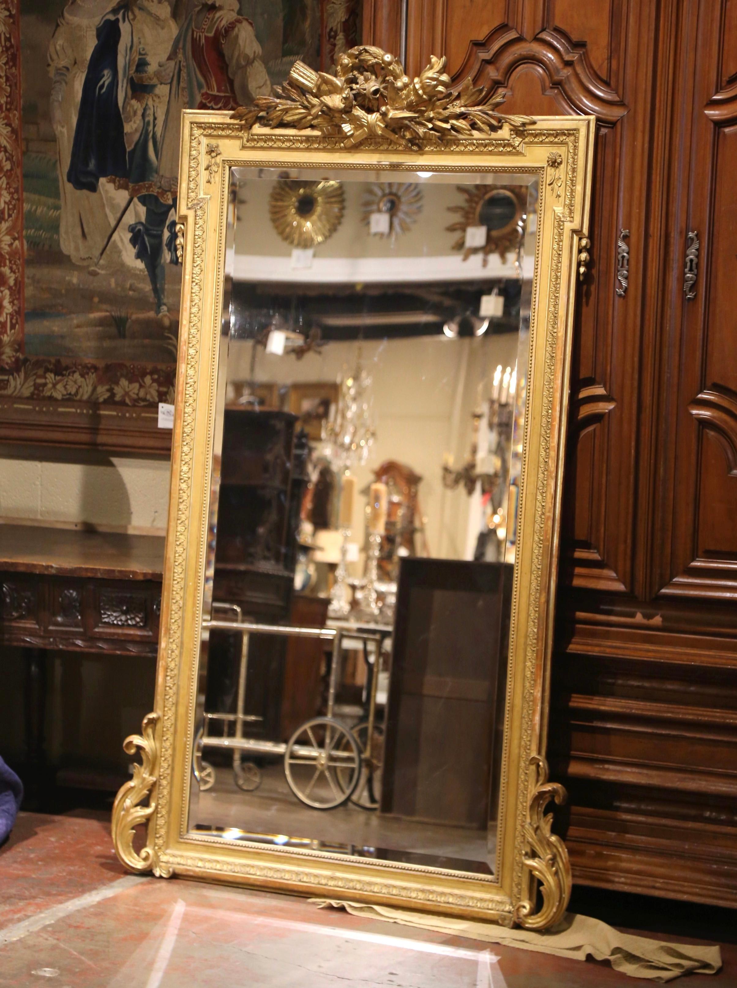 Vesti un caminetto con questo imponente specchio dorato antico! Realizzato in Francia intorno al 1870 e alto più di due metri, lo specchio rettangolare con angoli a rosetta è decorato con un intricato cartiglio sul frontone con una corona centrale
