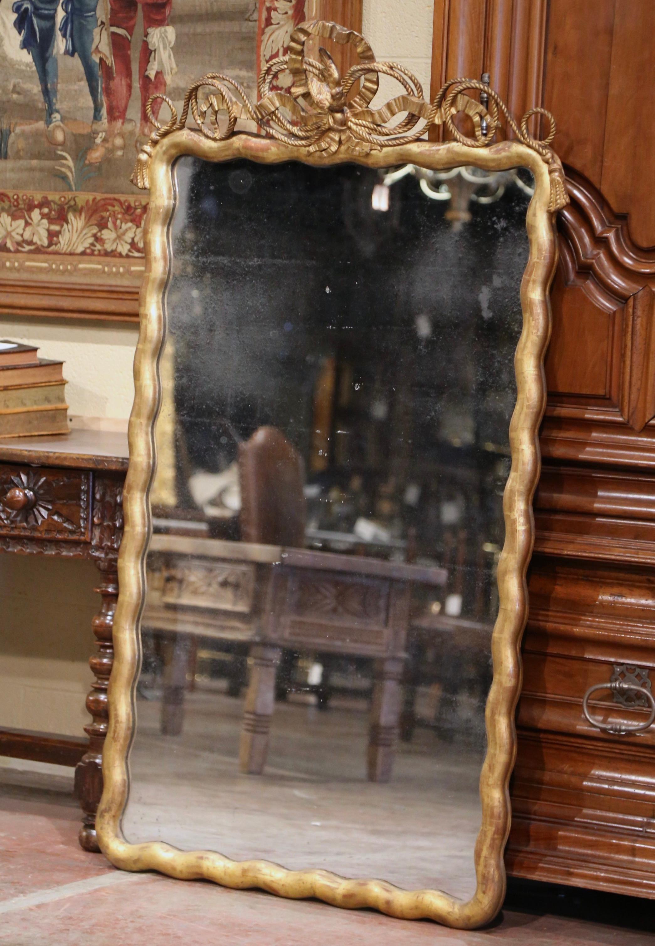 Dress a mantel or a living room with this antique gilt mirror. Crafted in France circa 1870, the tall rectangular mirror is decorated with a hand carved bird motif in high relief at the pediment, over the traditional Louis XVI ribbon bow ending with
