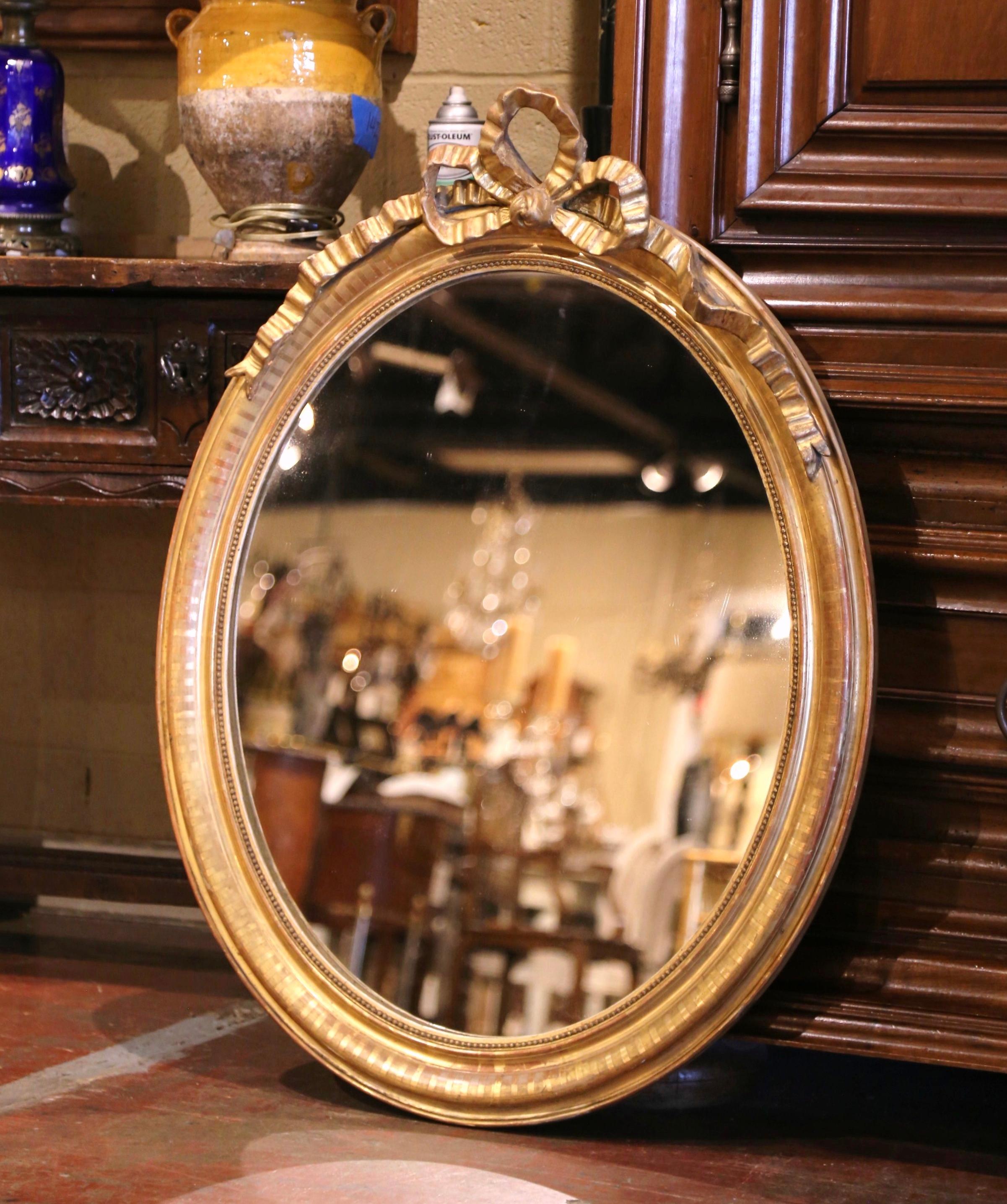 Decorate a powder room or entryway with this elegant antique wall mirror. Crafted in France circa 1880, the oval frame is decorated with the traditional Louis XVI ribbon bow at the pediment, and embellished with discrete strip motifs around the