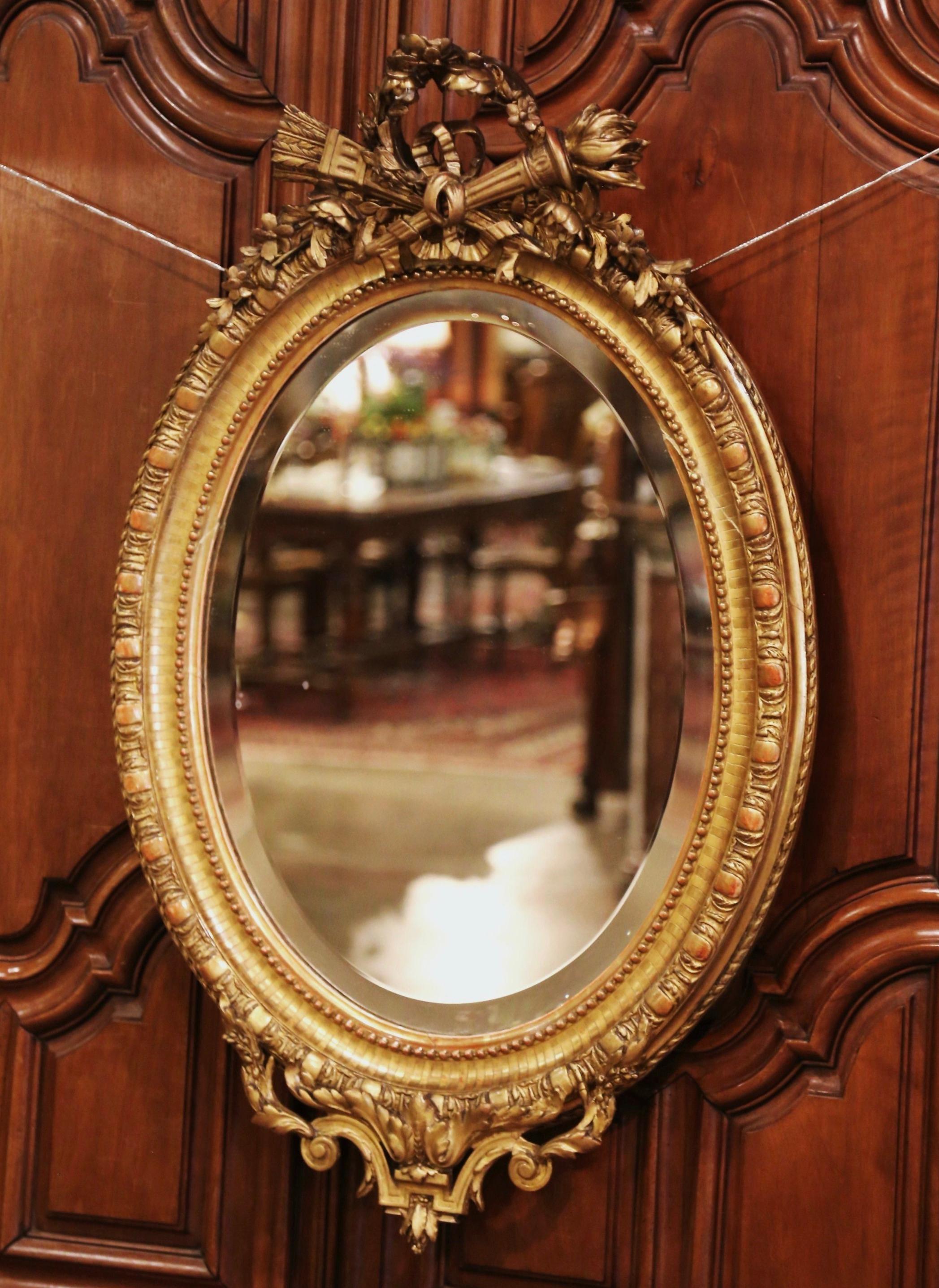 Decorate a powder room or entryway with this elegant antique wall mirror. Crafted in France, circa 1860, the beaded oval frame is decorated with floral motifs including torch decor and the traditional Louis XVI ribbon bow at the pediment, and