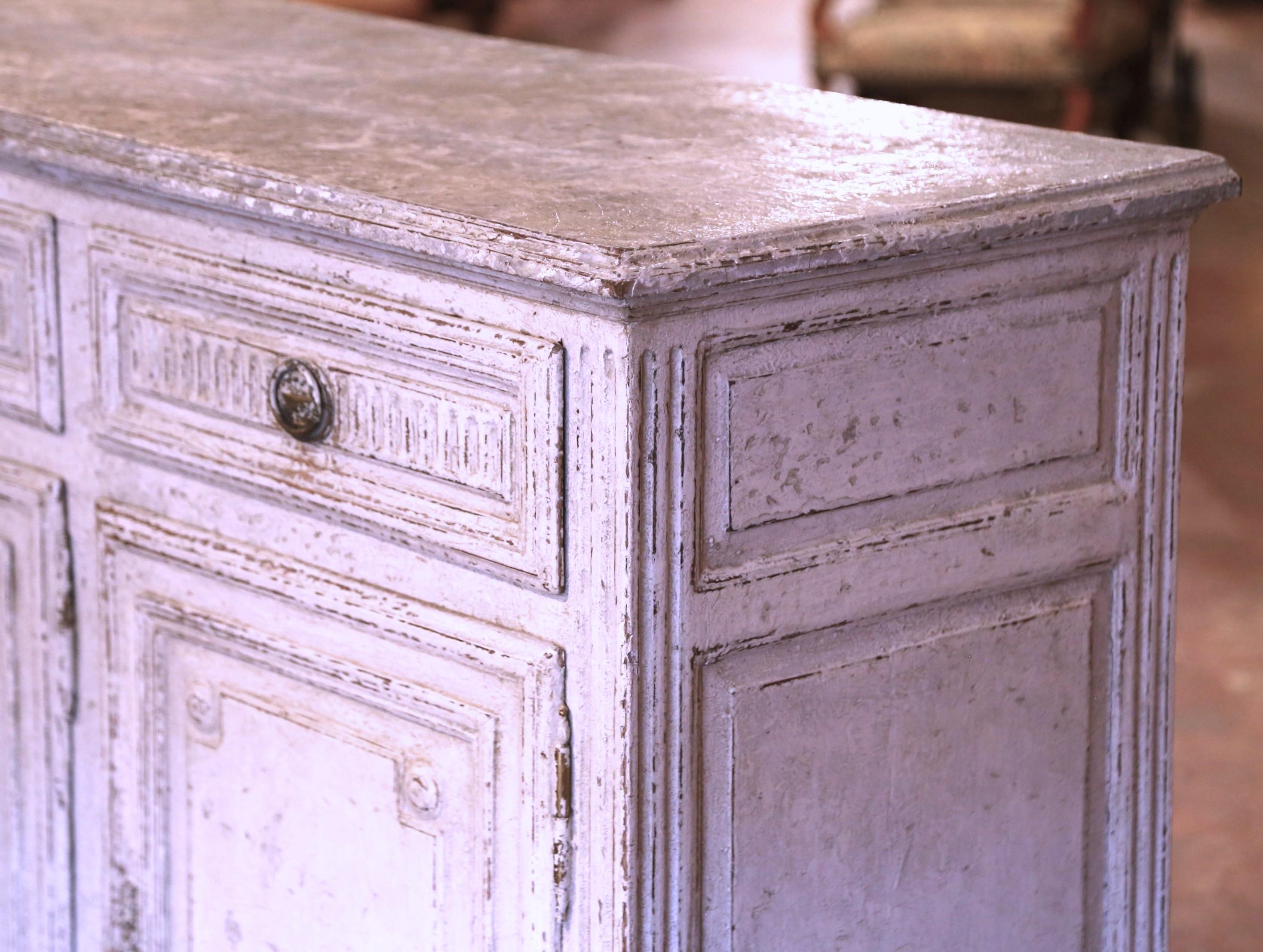 Dress a dining room or a den with this elegant antique painted buffet. Crafted in France circa 1870, the sideboard stands on tapered legs over a carved and straight plinth apron. The traditional enfilade is fitted with three carved drawers across