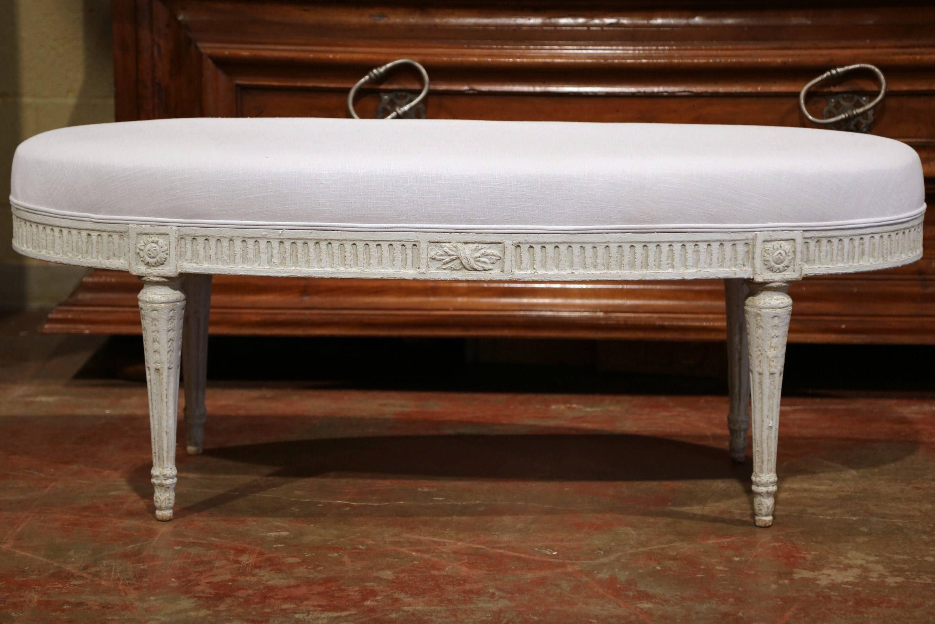 Complete your entryway, living room or bedroom with this grey painted bench from France, created circa 1890. Oval in shape, the antique features a carved design around the apron, which includes flower medallions and four fluted legs. The classic