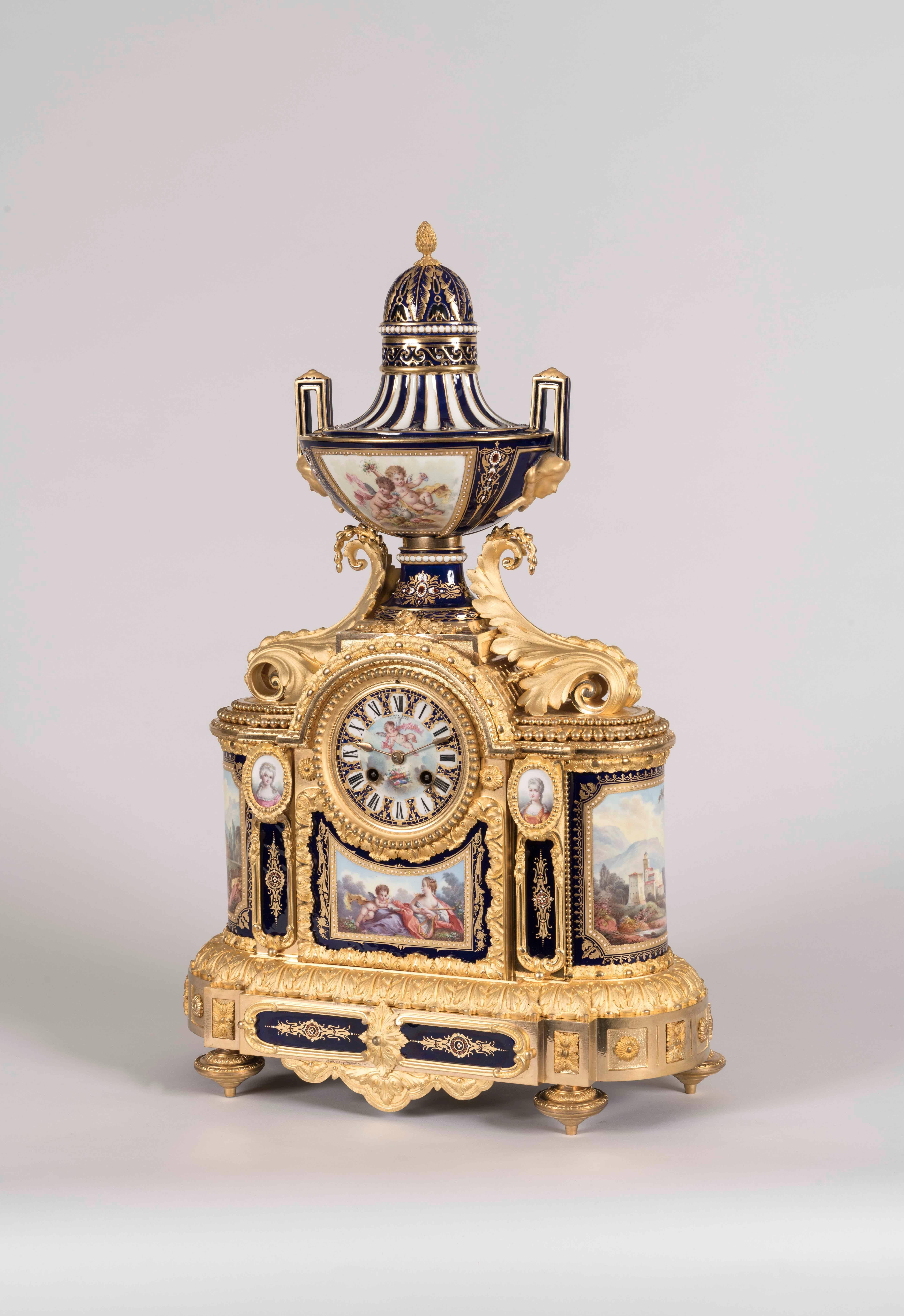 Eine Garniture de Chemineé nach dem Geschmack von Louis XVI
Von Arnold & Lewis (später Simmons)

Die Manteluhr und die beiden dazugehörigen Vasen sind aus juwelenbesetztem Porzellan im Sèvres-Stil gefertigt, von Hand und polychrom verziert, mit