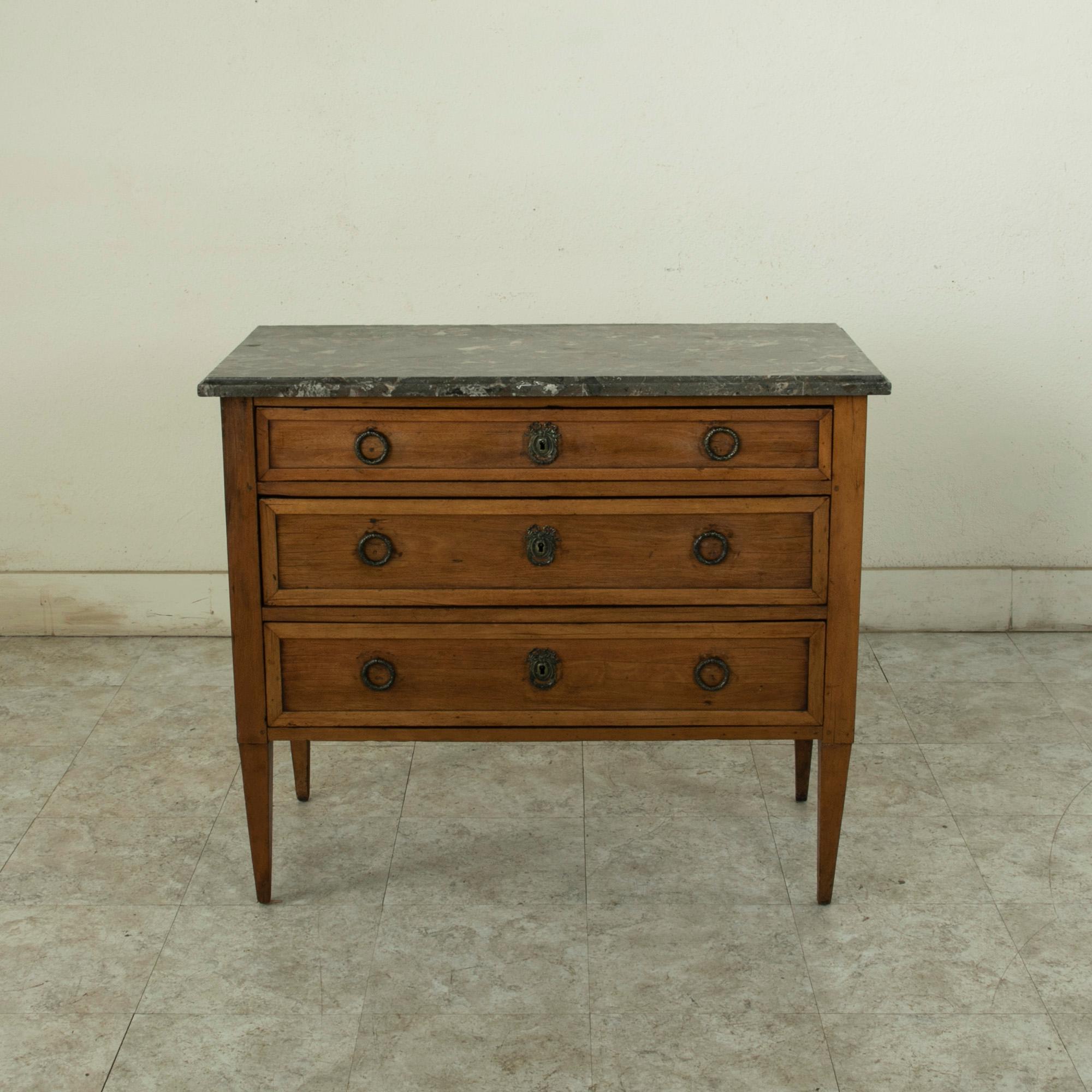 This small scale French Louis XVI style commode or chest from the late 19th century is constructed of solid fruitwood and features a beveled marble top. The cabinet has solid paneled sides and drawer fronts. Three drawers of dovetail construction