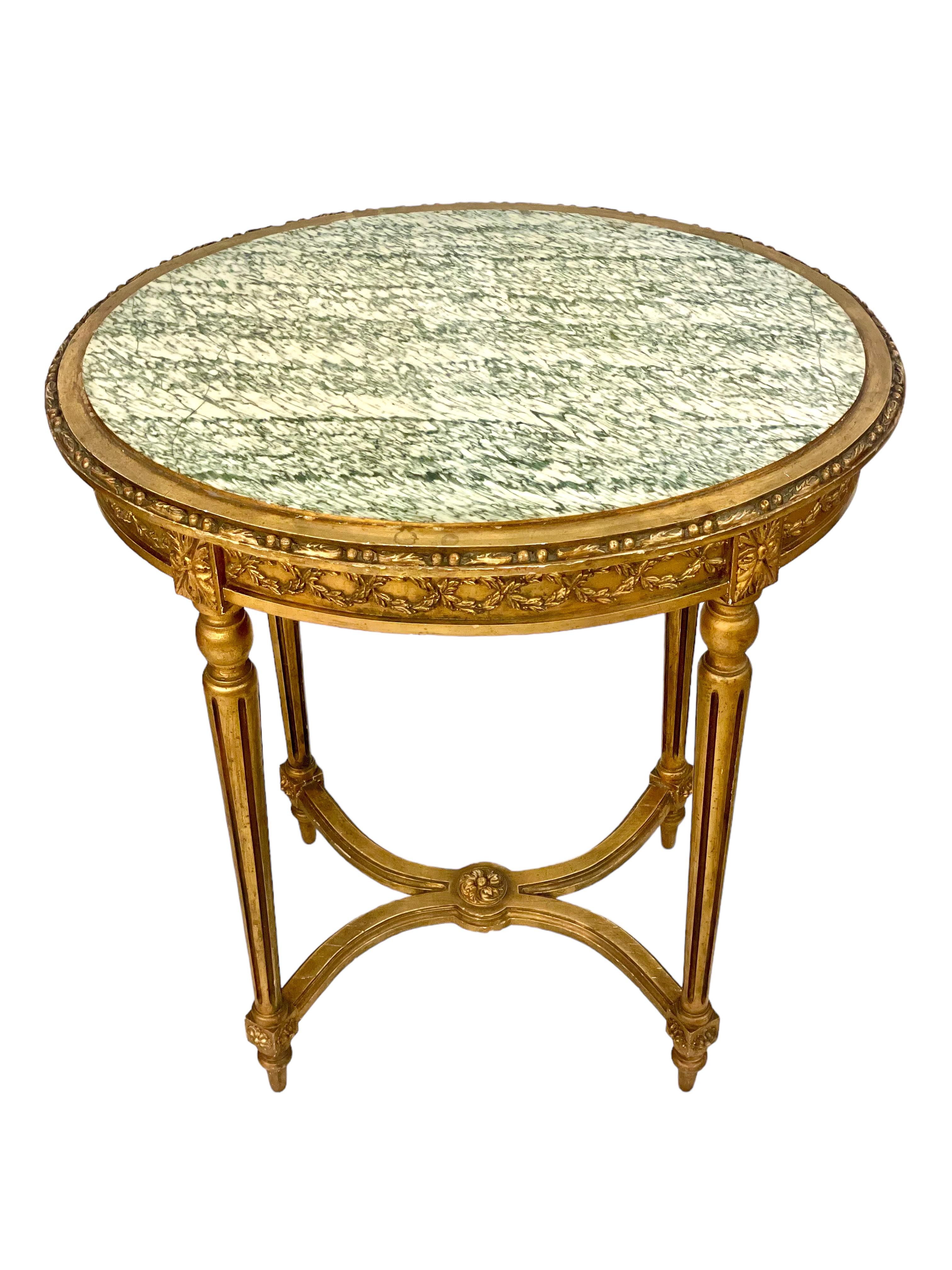 A very decorative Louis XVI-style Napoleon III center or side table in carved and gilded wood, and featuring an oval grey-green veined marble top. This pretty little table dates from the 19th century, and boasts abundant and exquisite carvings in