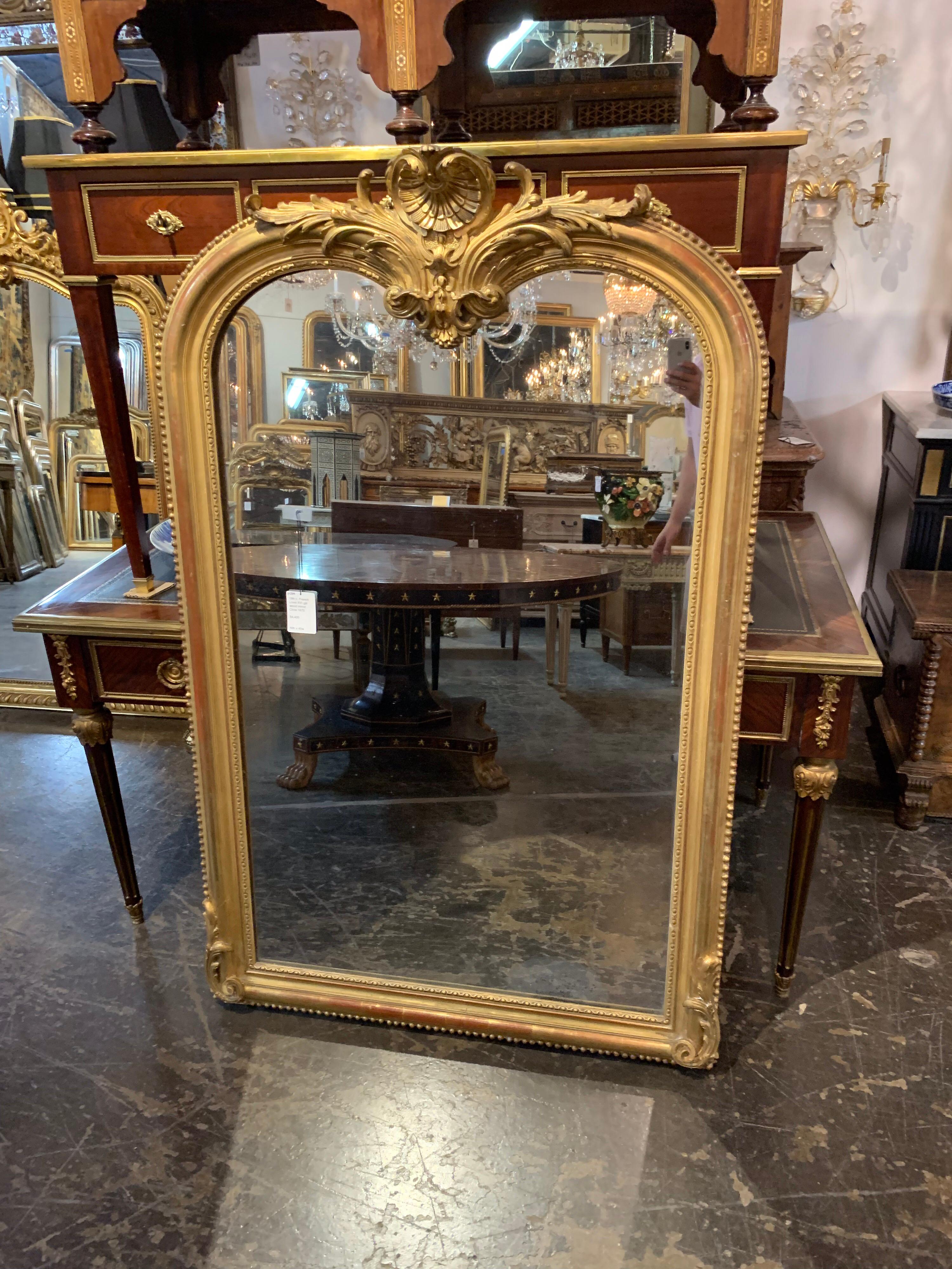 Extraordinary 19th century French Louis XVI giltwood mirror. The mirror is topped with an ornate carving of scrolls and shells, with beaded details around the border. A beautiful statement piece that will reflect light in the entire room.