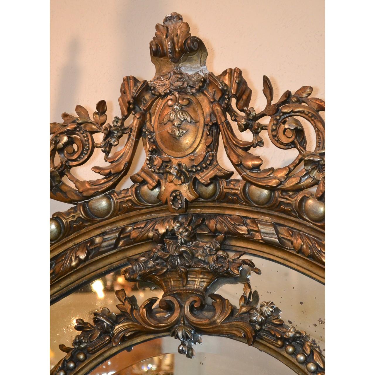 Outstanding 19th century French Louis XVI style giltwood and beveled edged wall or console mirror. The crest with a boldly carved leaf spray atop scrolling acanthus, laurel leaves, and songbirds. The oval inner frame decorated with a basket of