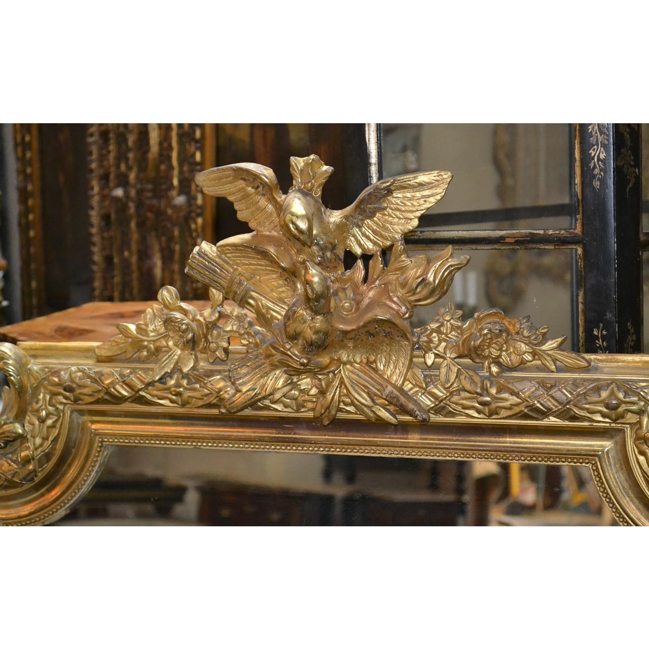 Fine quality 19th century French giltwood wall or console mirror with a shaped crest depicting carved eagles atop the Royal symbols of Louis XVI, the flamed torch of truth and the arrows of justice. Accented with trailing vines and bold acanthus